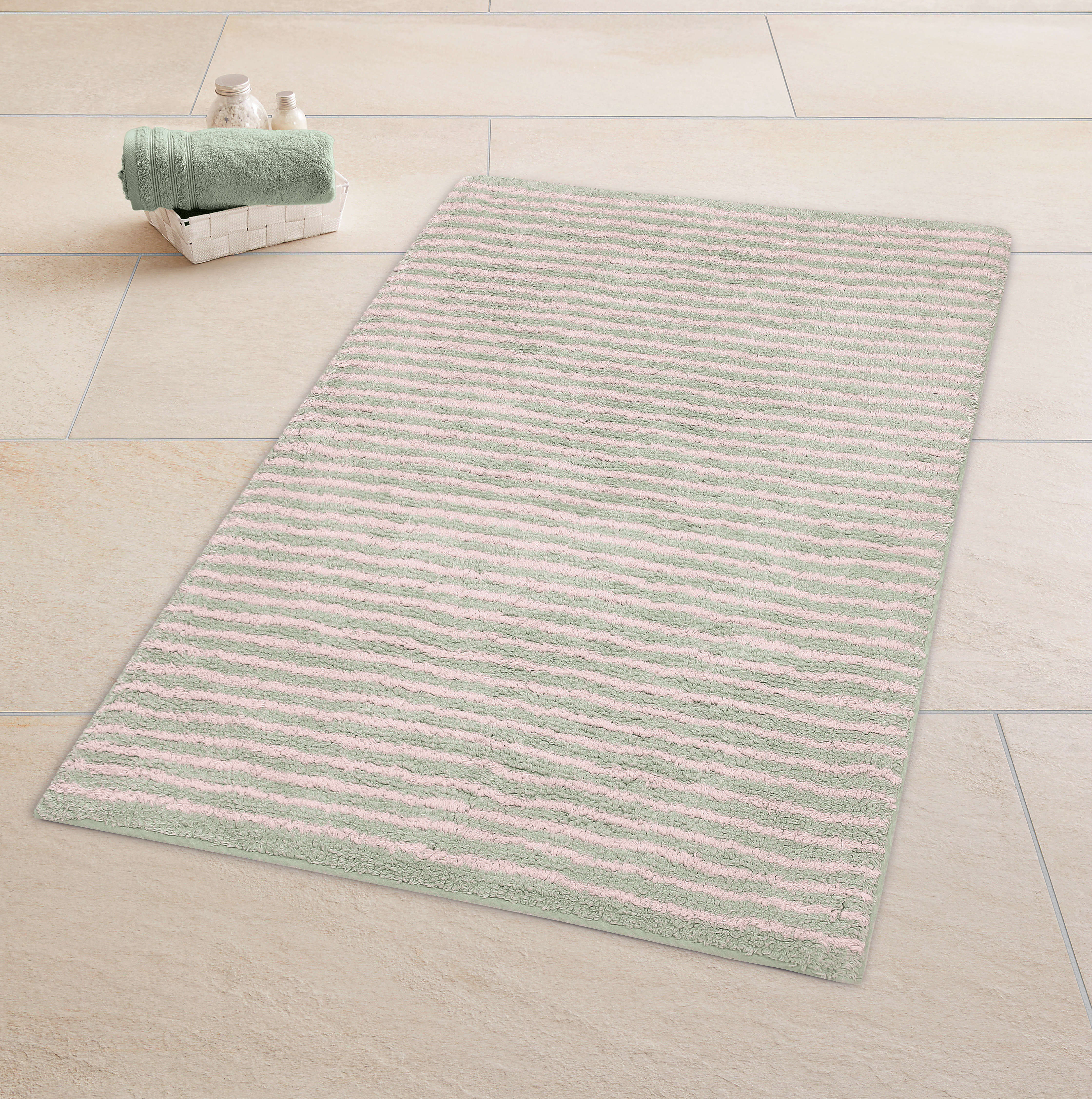 Weicher Badteppich in Pastellfarben mit Streifenmuster, dekoriert mit Handtüchern und Pflegeprodukten in einem Korb.