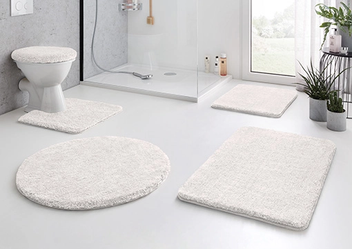 Weißes Badematten-Set in modernem Badezimmer, bestehend aus runder, rechteckiger und WC-Matte, weich und stilvoll.