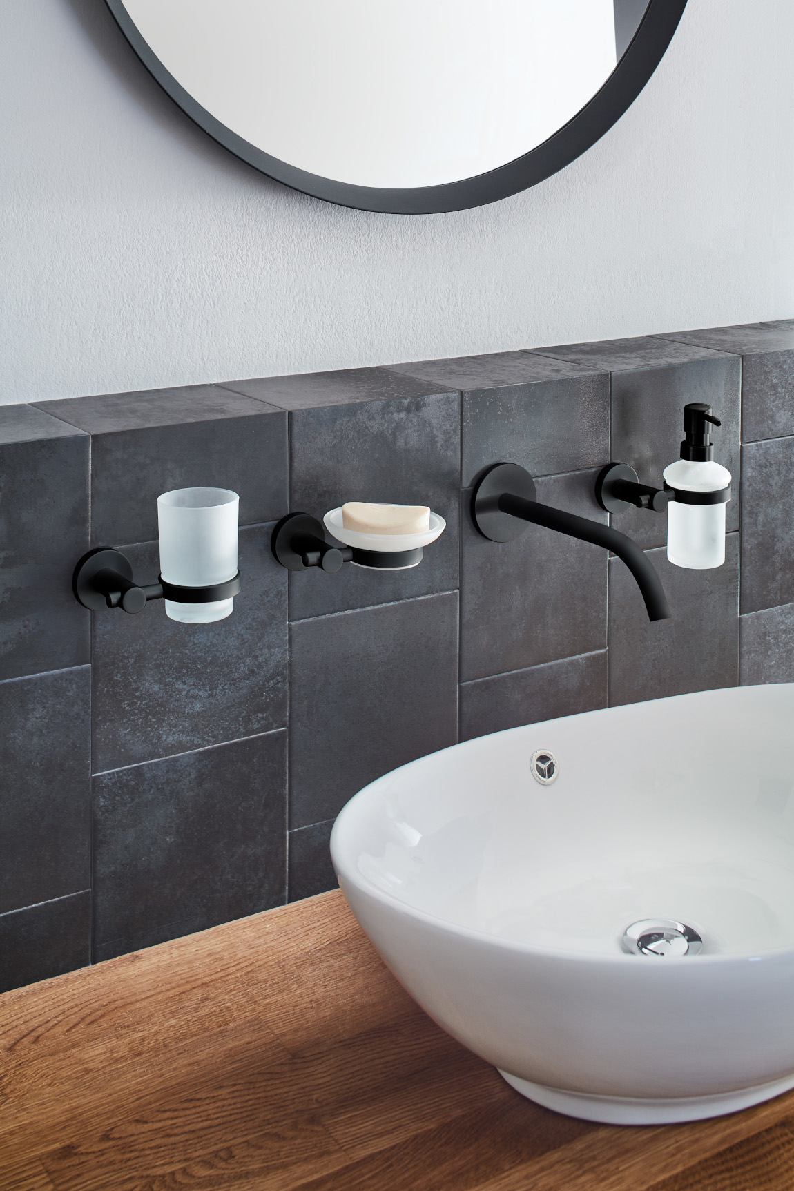 Modernes Badezimmer mit schwarzem Wandzubehör, weißem Waschbecken und Holzarbeitsplatte. Elegantes Design mit Spiegel und grauen Fliesen.