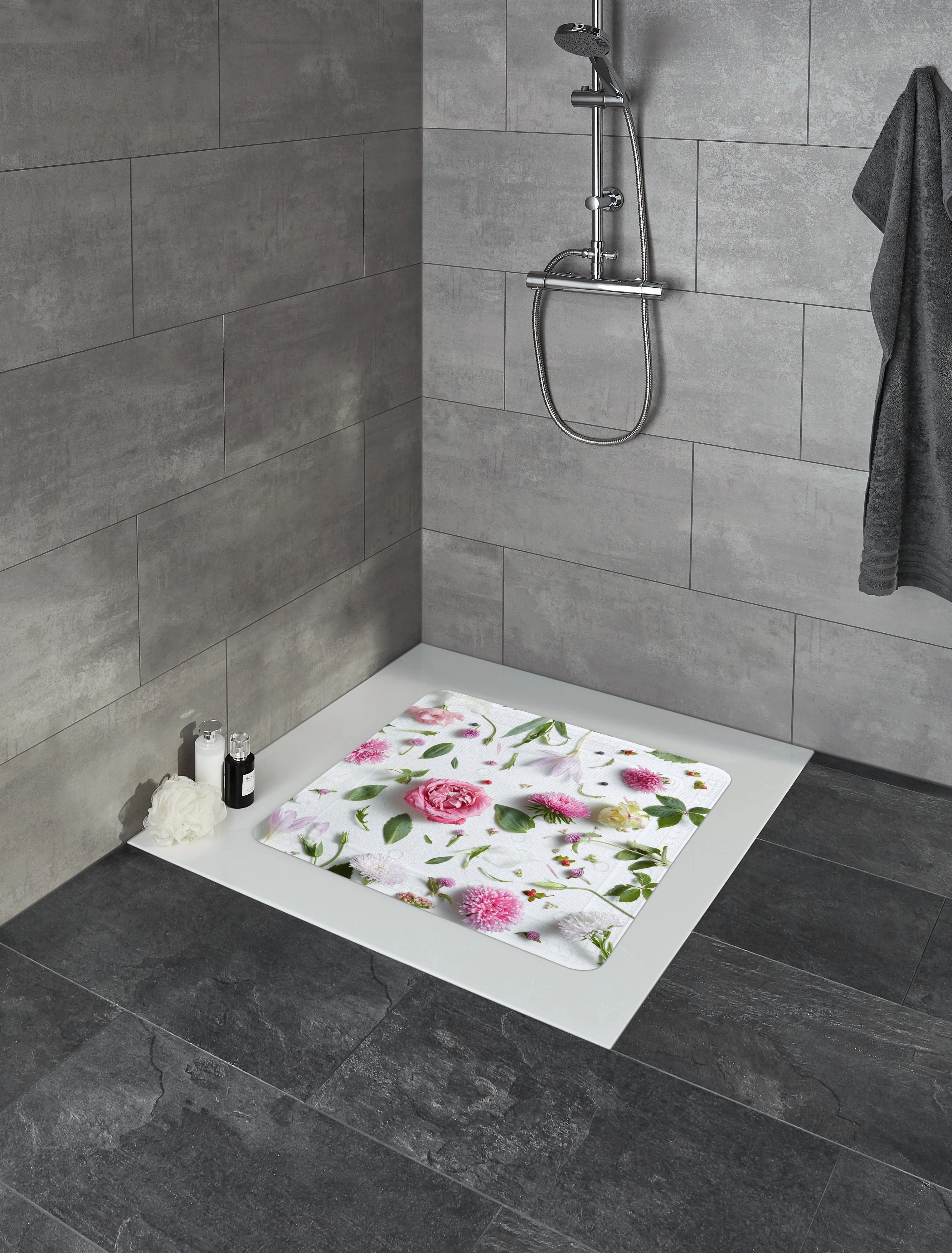 Duschmatte mit floralem Design in einer modernen, grauen Dusche. Weiße und rosa Blumenmuster auf weißem Hintergrund.