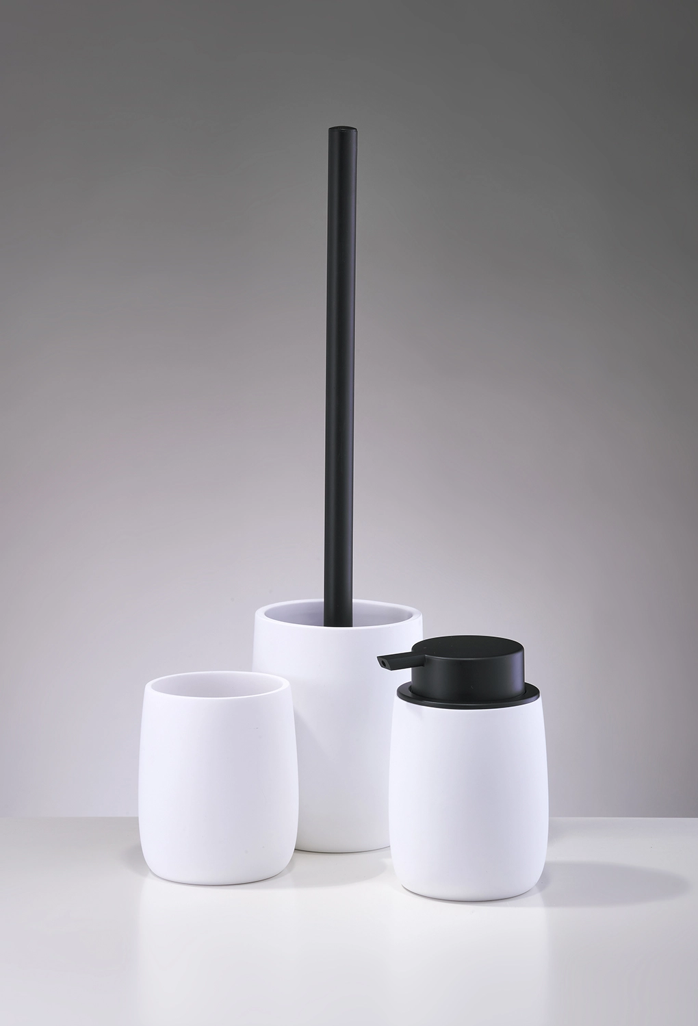 Weißes Badezimmer-Set bestehend aus Seifenspender, Zahnbürstenhalter und Toilettenbürste mit schwarzem Griff.