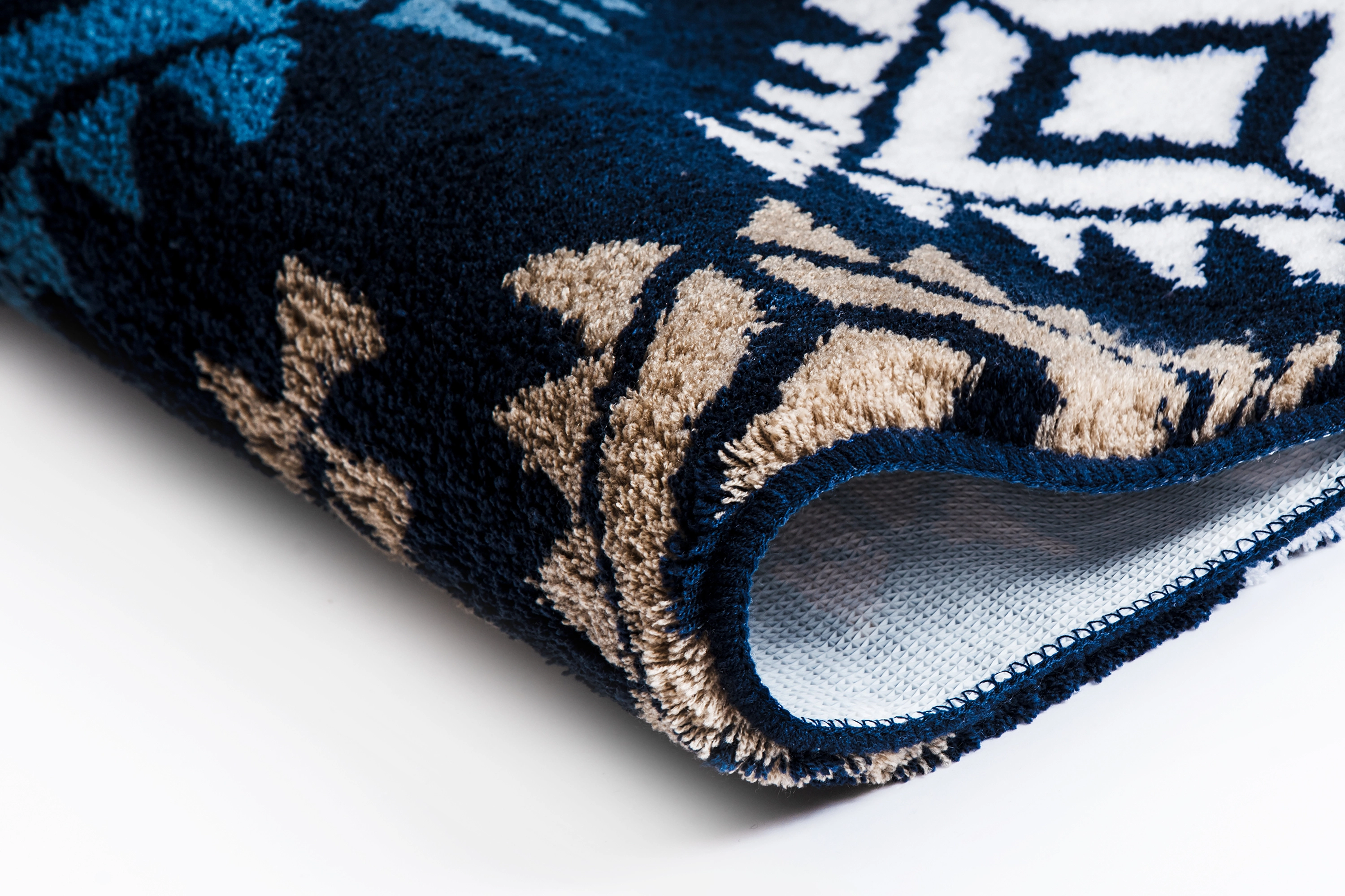 Badezimmerteppich mit geometrischem Muster in Blau- und Beigetönen, weiche Textur, Nahaufnahme der Kante.