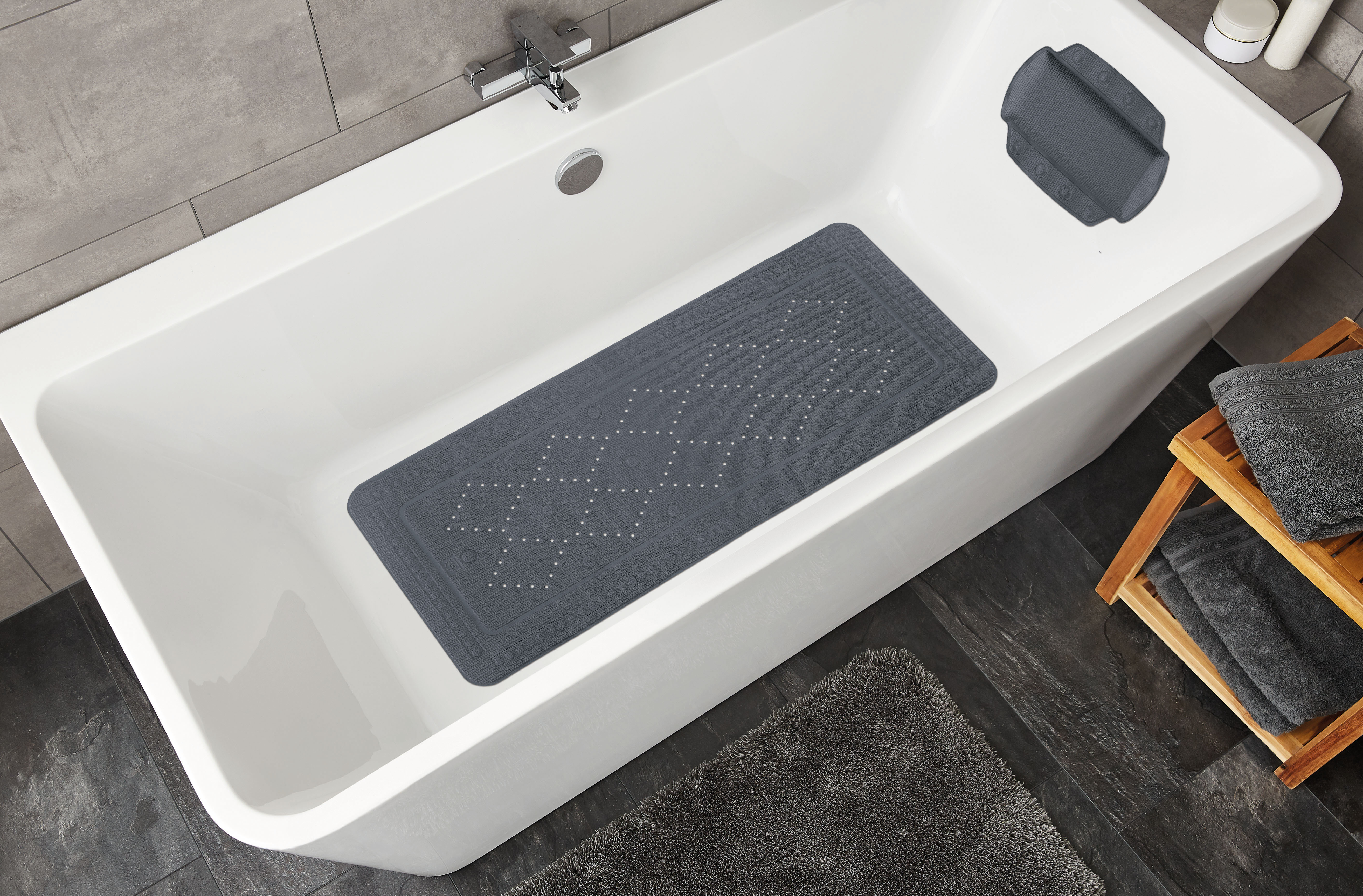 Graue Badewannenmatte mit rutschfestem Muster in moderner Badewanne, umgeben von Handtüchern und Badaccessoires.