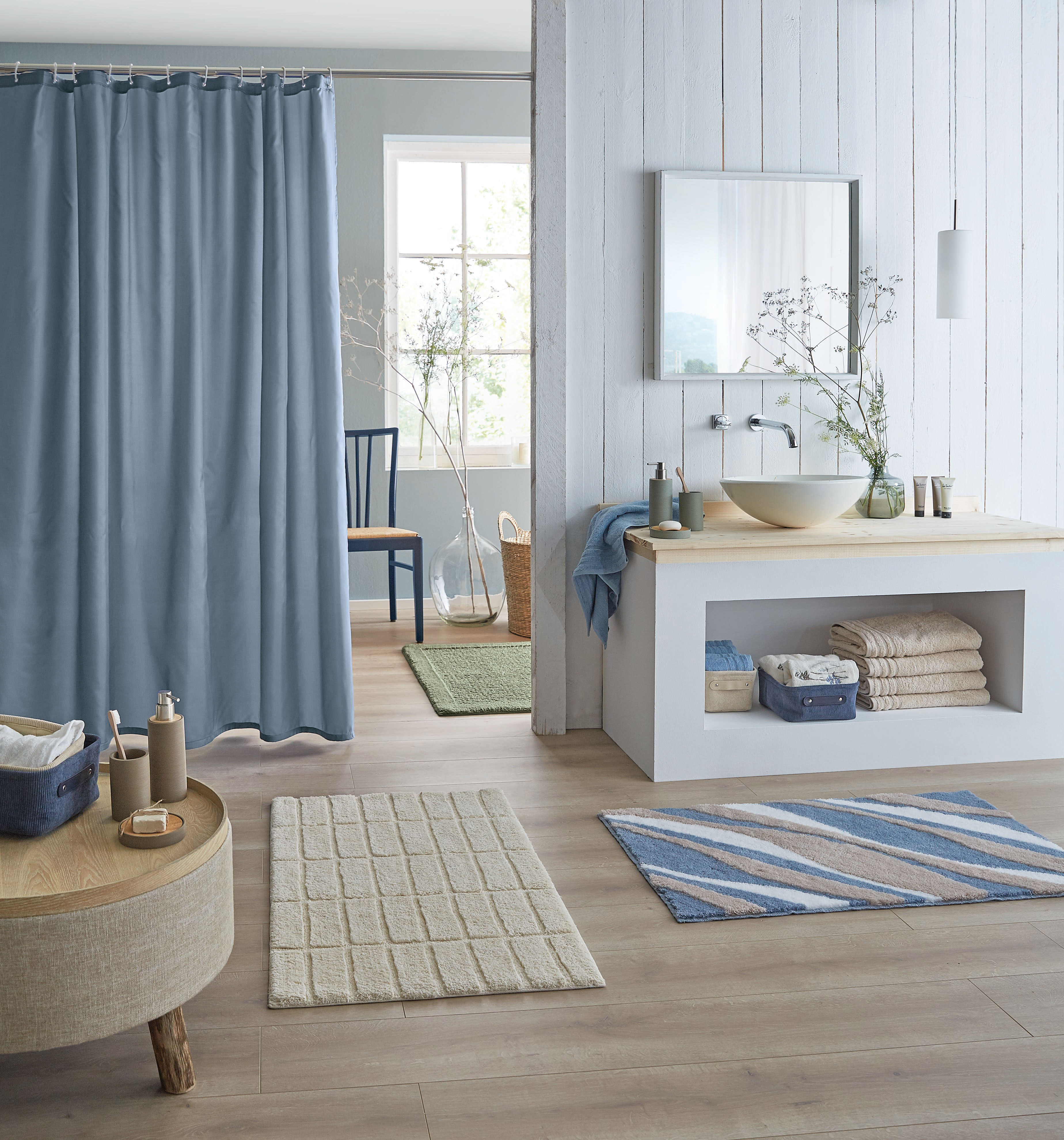 Modernes Badezimmer mit blauen und beigen Akzenten, Duschvorhang, Teppichen und stilvollen Accessoires.