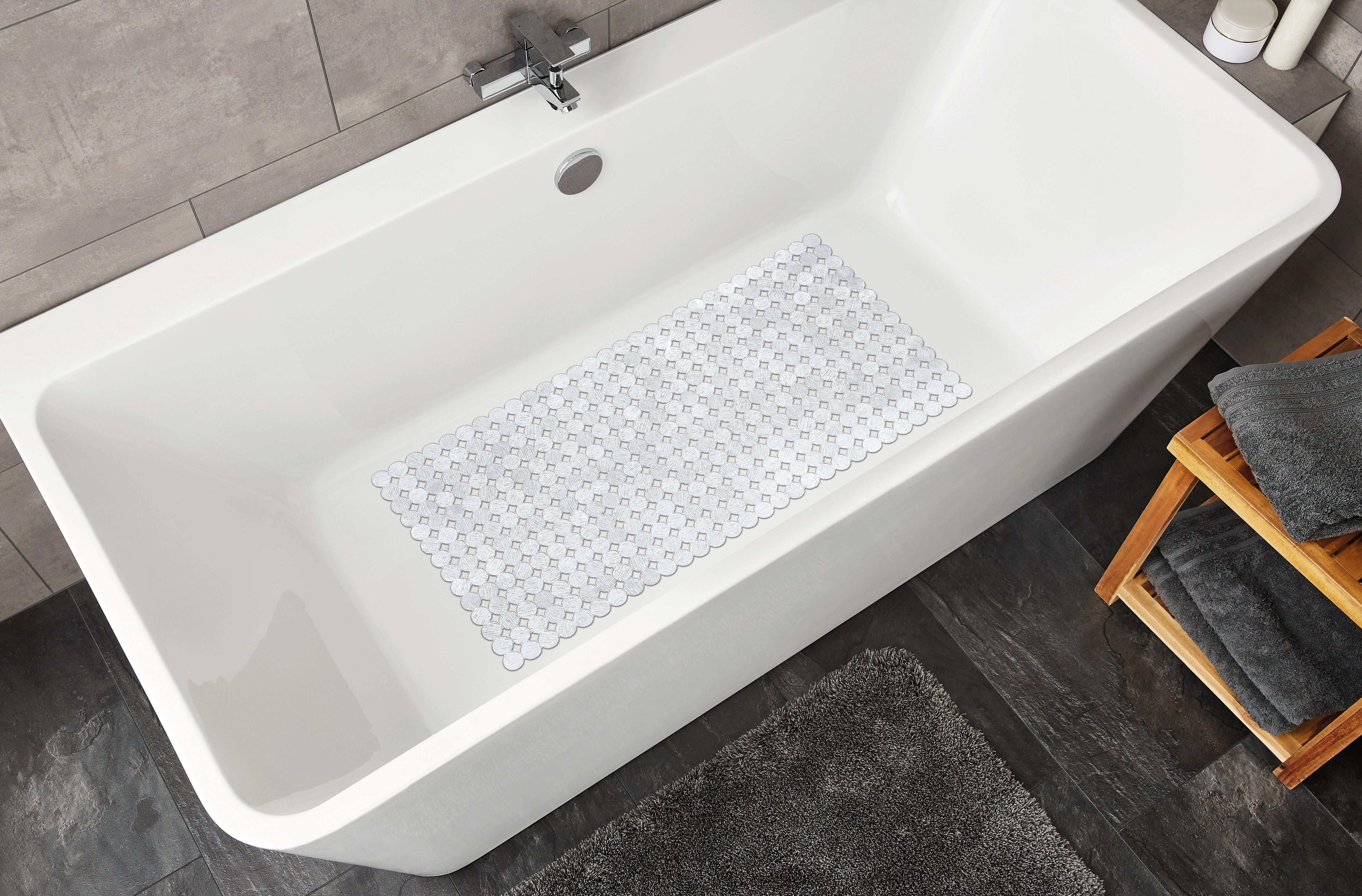 Rutschfeste Badematte in Weiß in einer modernen Badewanne, umgeben von grauen Handtüchern und einem Holzregal.