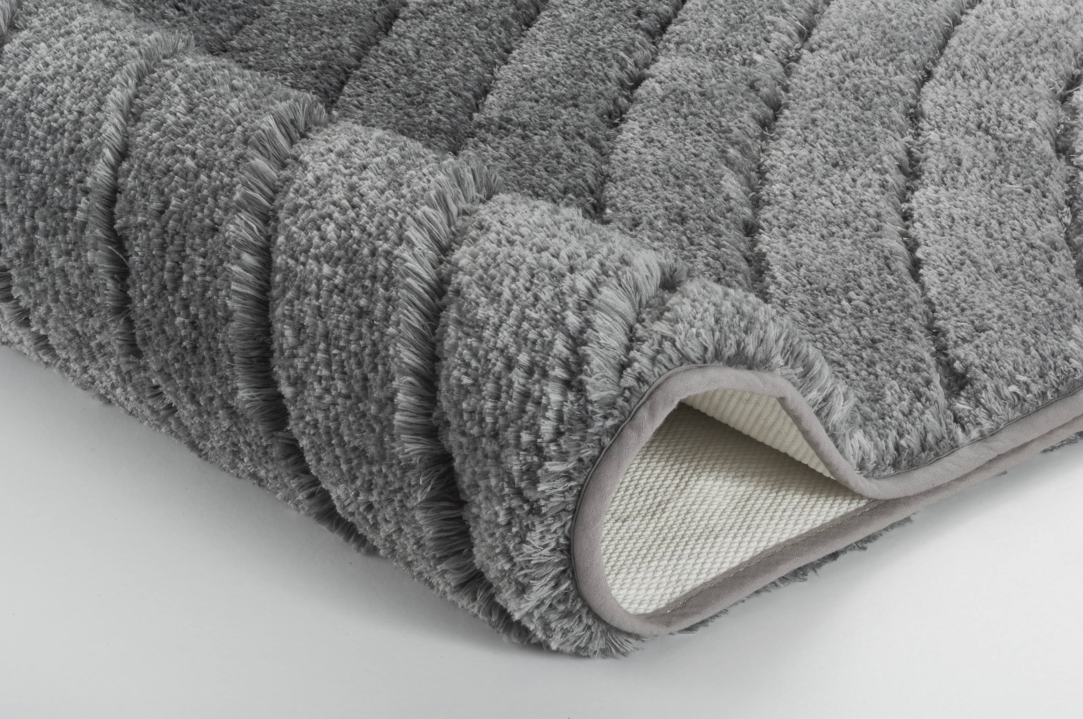 Grauer, flauschiger Badteppich mit rutschfester Unterseite, ideal für ein gemütliches und sicheres Badezimmer.