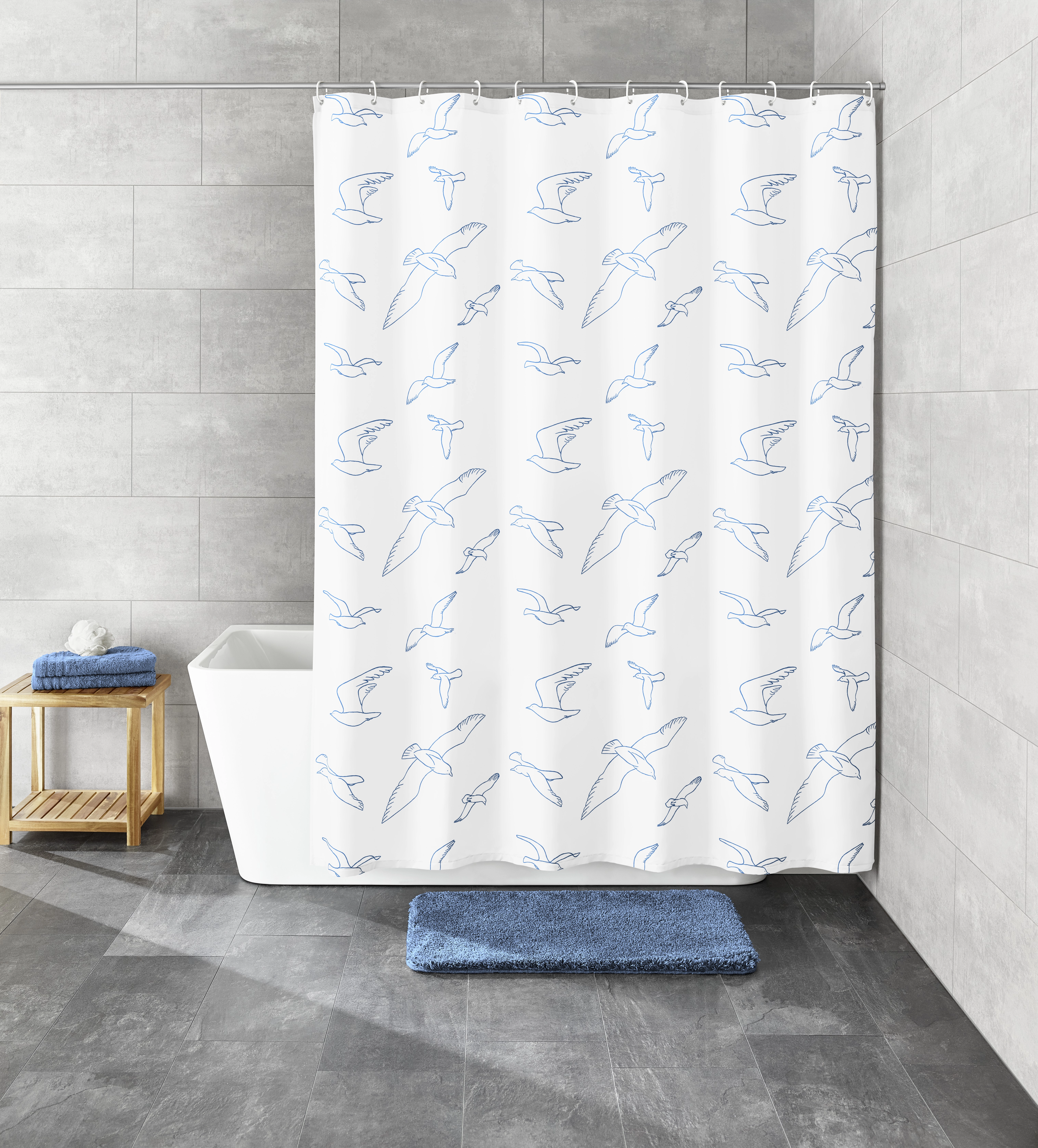 Duschvorhang mit blauem Vogelmuster, modernes Badezimmer, graue Fliesen, weiße Badewanne, blauer Badteppich, Holzregal.