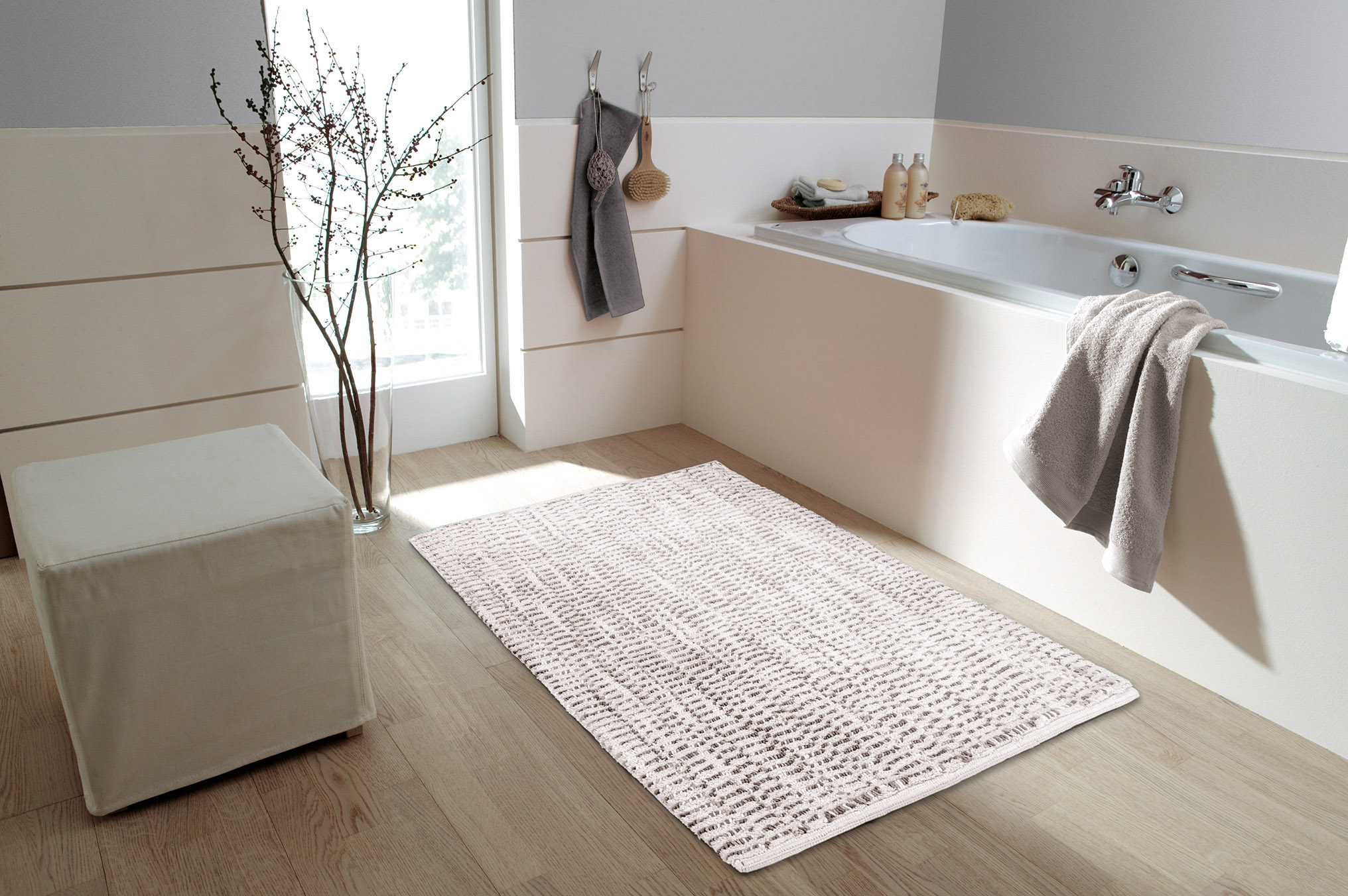 Moderner Badezimmerteppich in Beige mit dezentem Muster, platziert vor einer Badewanne in einem stilvoll eingerichteten Badezimmer.