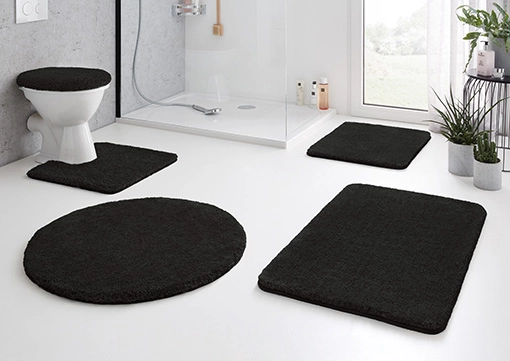 Schwarze Badematten-Set in modernem Badezimmer, bestehend aus runden und rechteckigen Matten sowie einem WC-Deckelbezug.