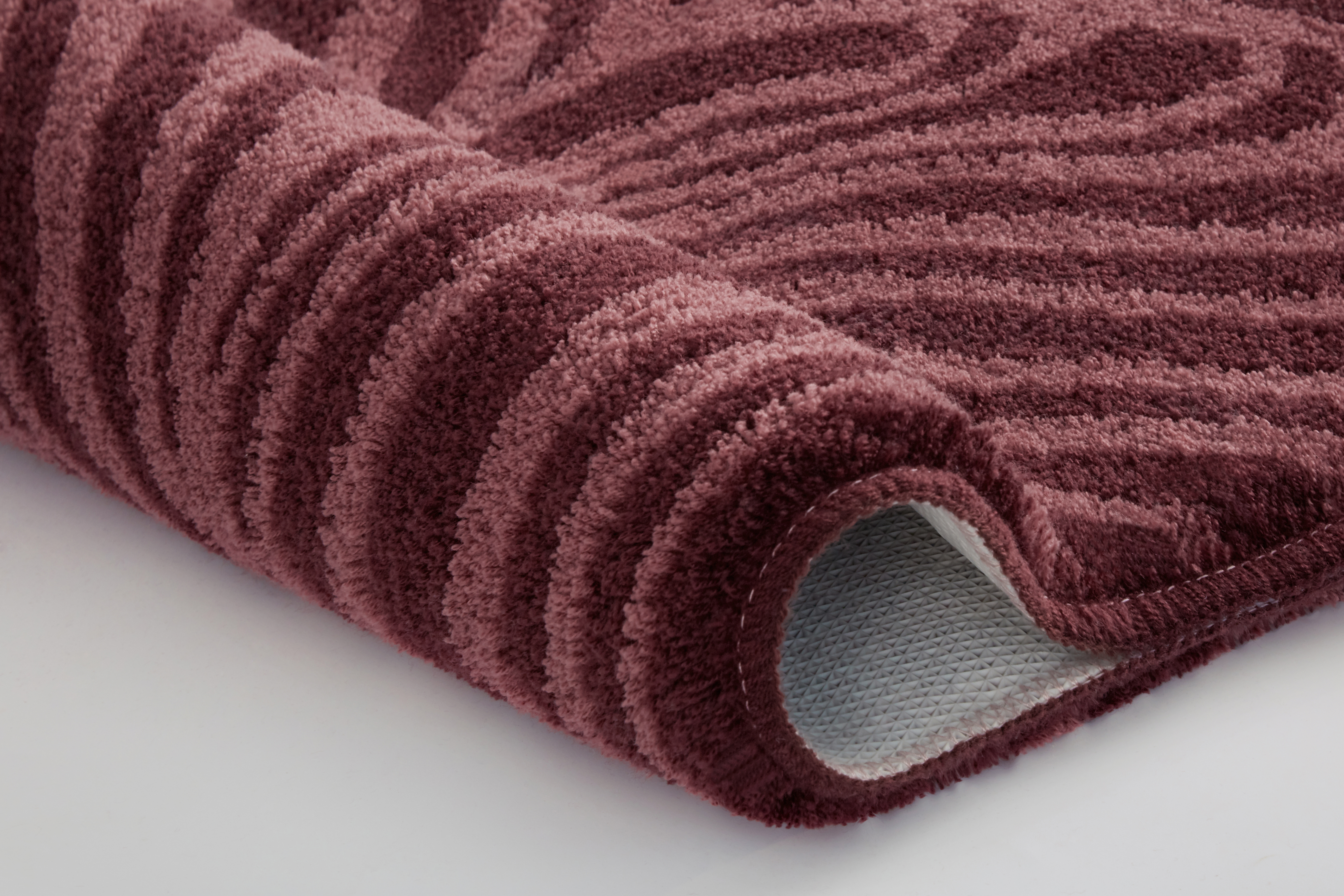 Weinroter Teppich mit wellenförmigem Muster, weiche Textur, aufgerollt, zeigt die Rückseite. Ideal für Wohn- und Schlafzimmer.