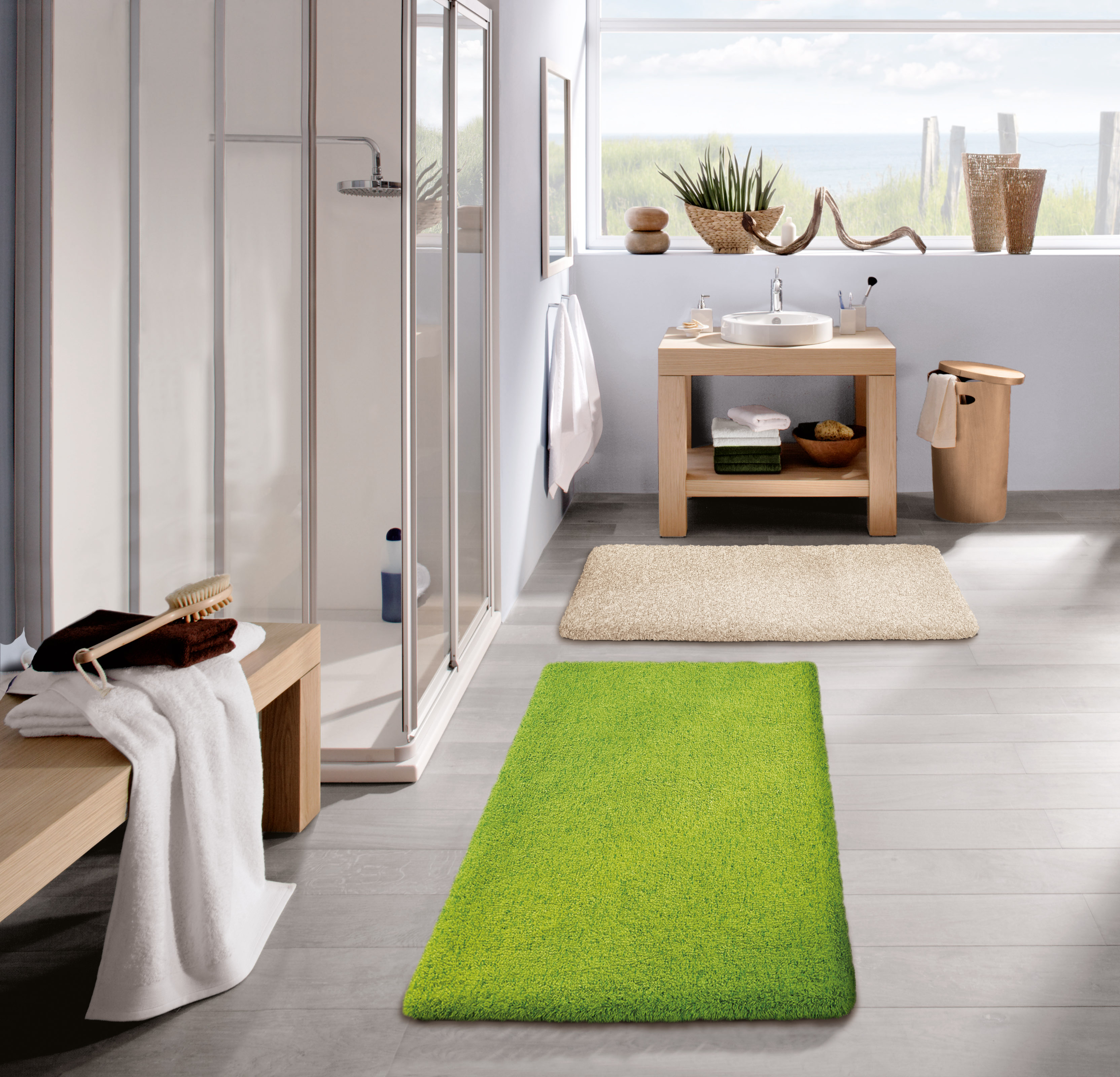Modernes Badezimmer mit grüner und beiger Badematte, Holzwaschtisch, Dusche und Fenster mit Blick auf die Dünen.