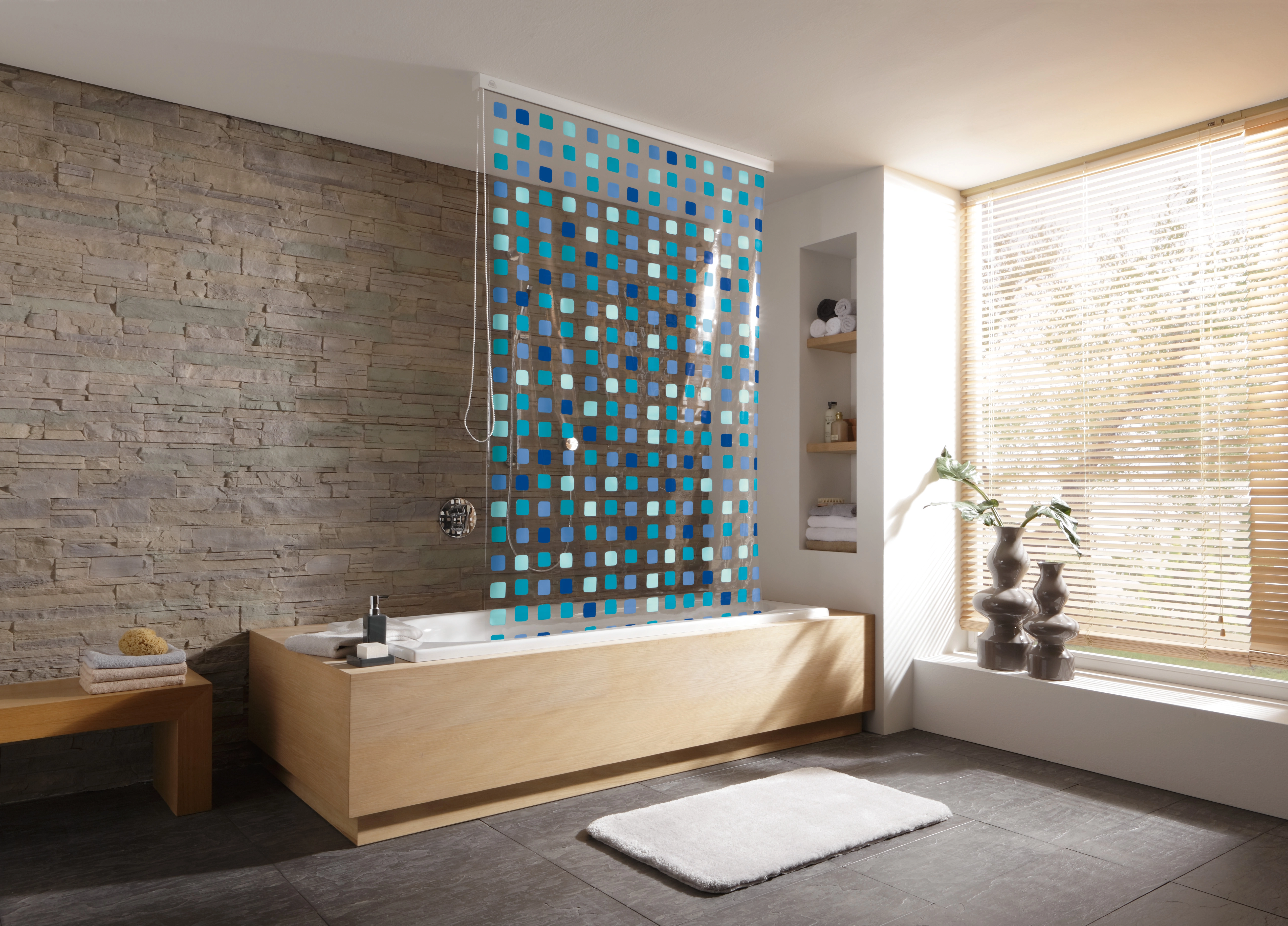 Moderne Badezimmergestaltung mit Badewanne, Duschvorhang mit blauem Muster, Steinwand und großen Fenstern.