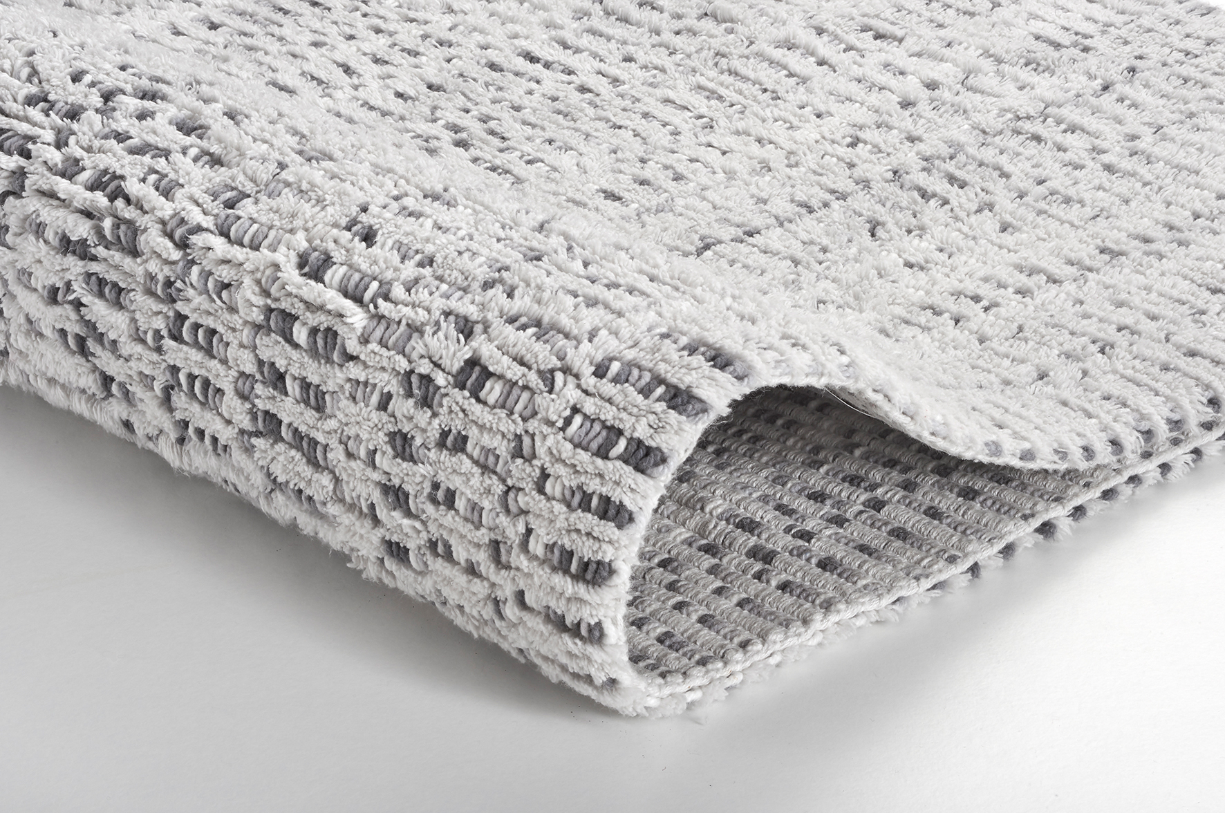 Weißer, flauschiger Badteppich mit grauem, rutschfestem Untergrund und strukturierter Oberfläche für ein modernes Badezimmer.