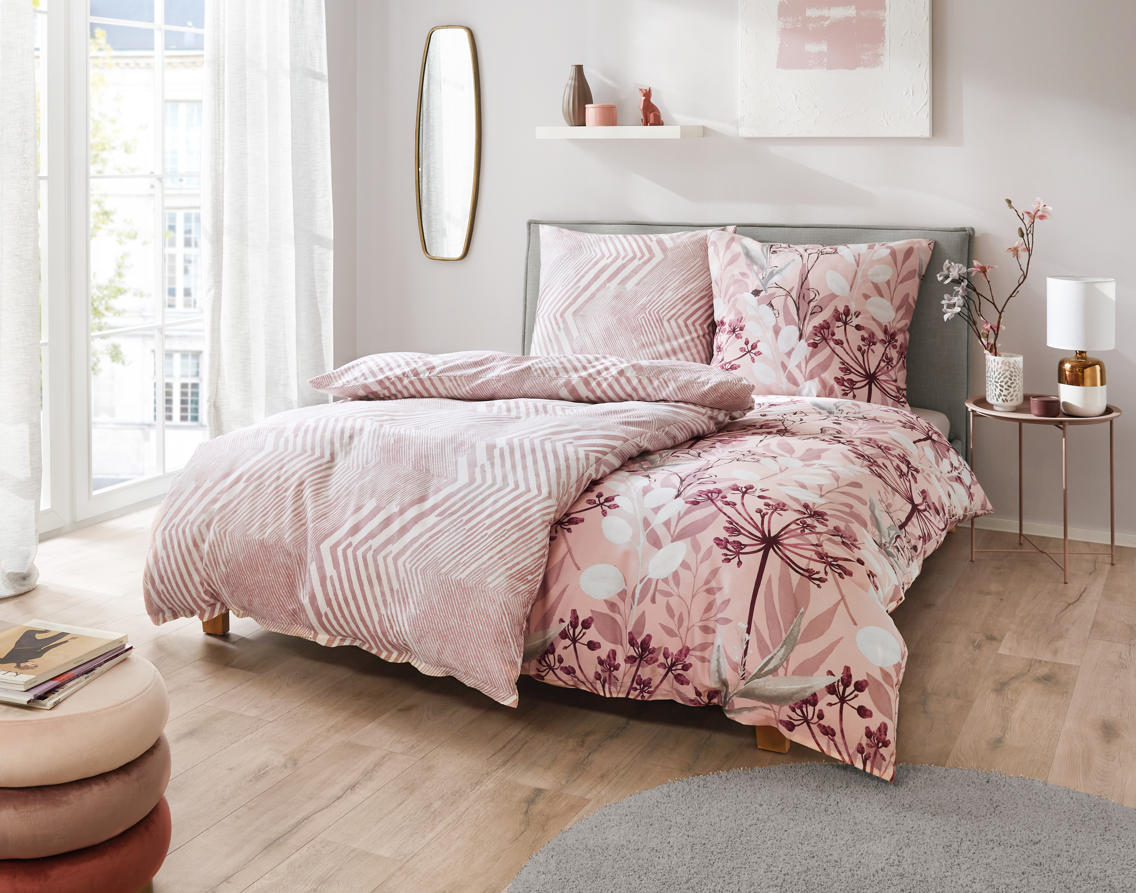 Gemütliches Schlafzimmer mit stilvoller Bettwäsche in Rosa- und Weißtönen, floralen und geometrischen Mustern, modern eingerichtet.