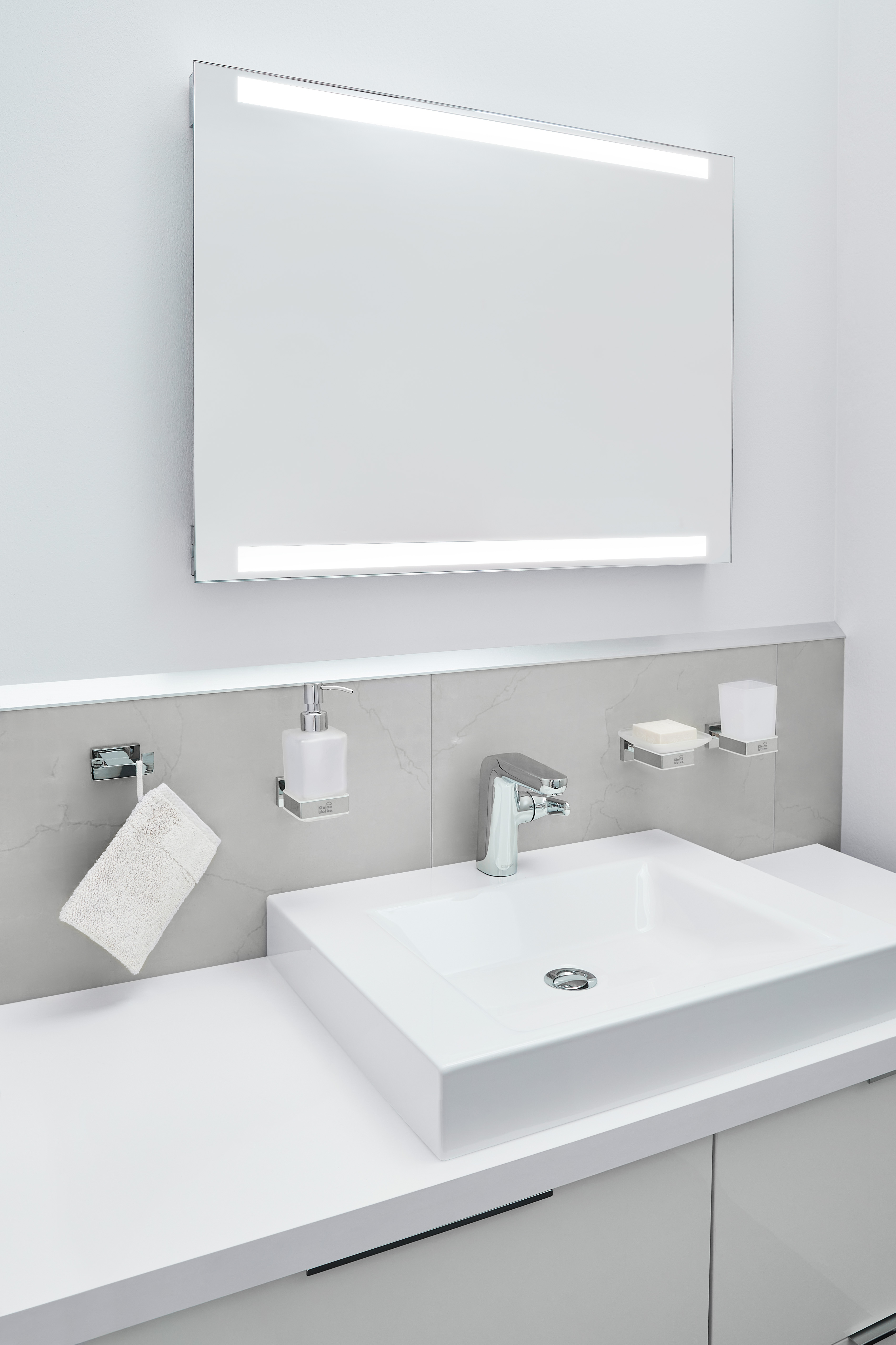 Modernes Badezimmer mit beleuchtetem Spiegel, weißem Waschbecken und eleganten Accessoires.