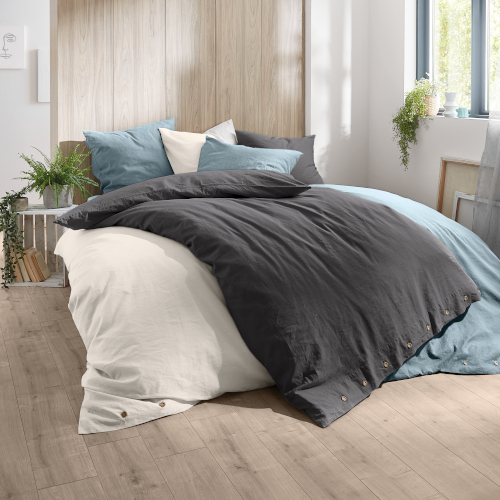 Bettwäsche-Set in Anthrazit und Creme, aus Baumwolle, mit Holzknöpfen, auf einem modernen Bett in einem hellen Schlafzimmer.