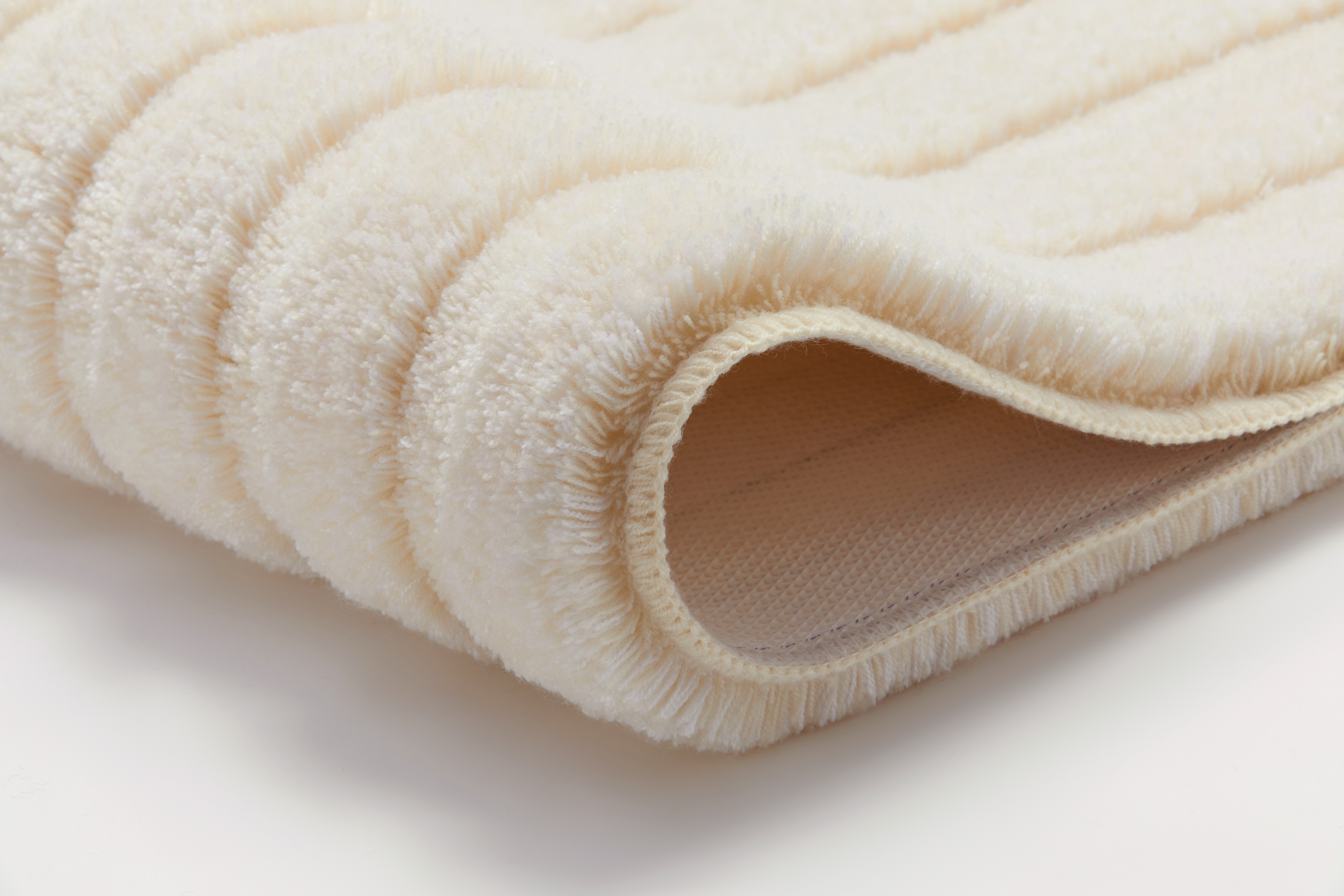 Weiche, cremefarbene Badematte mit geripptem Design und rutschfester Unterseite, ideal für ein gemütliches Badezimmer.