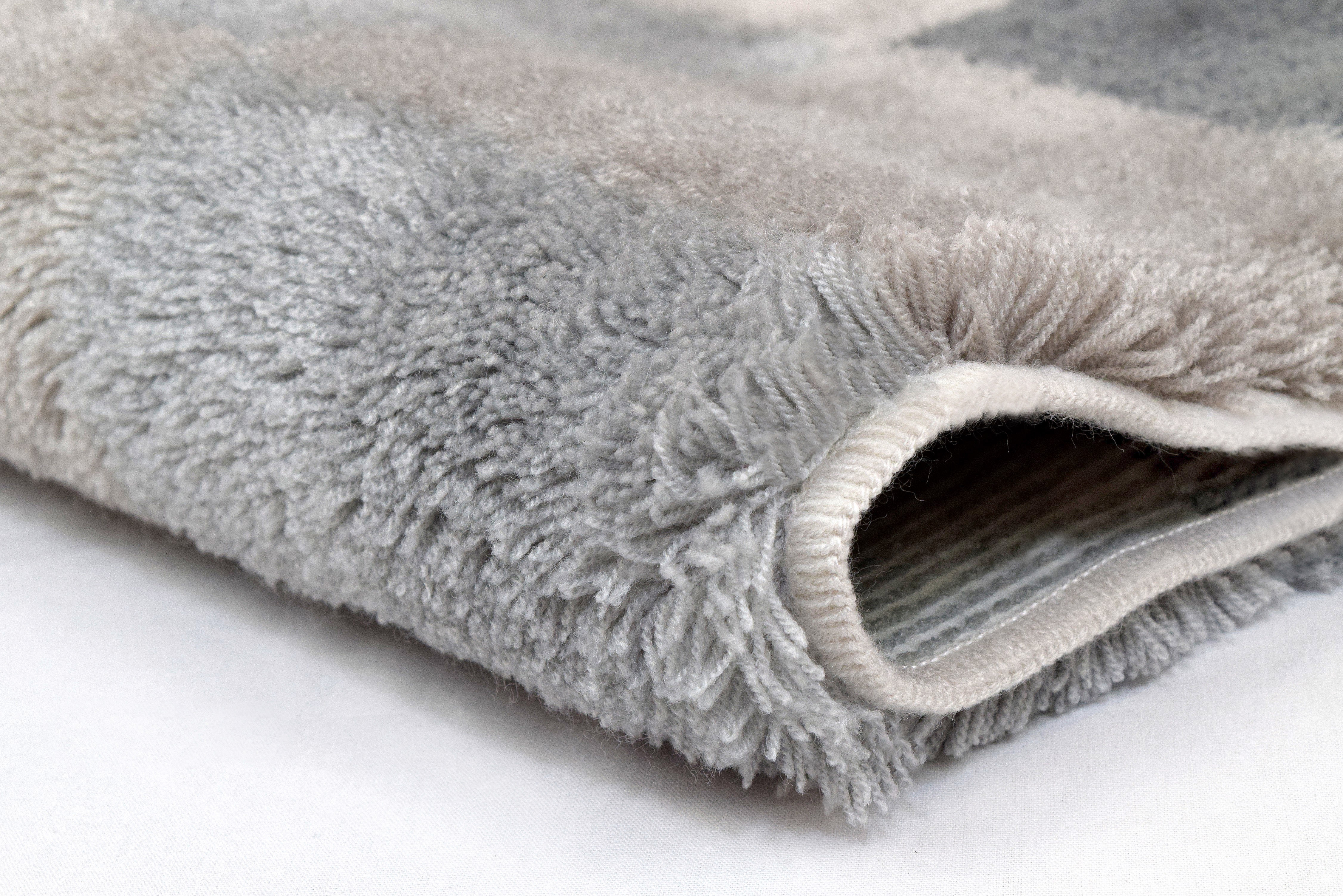 Weicher, grauer Badteppich mit flauschiger Oberfläche und rutschfester Unterseite, Nahaufnahme der Textur.