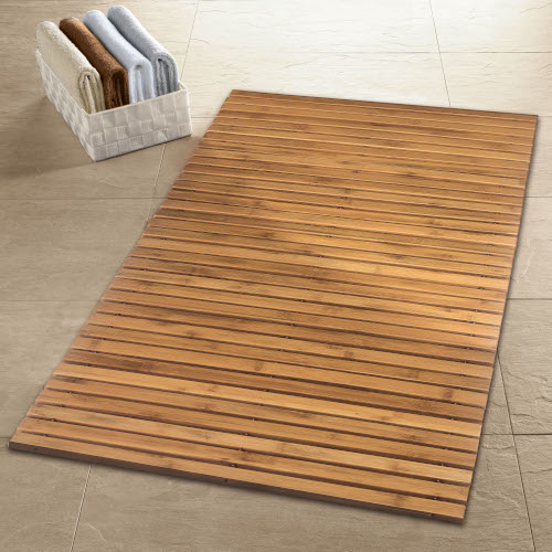 Holz-Badematte auf beigem Fliesenboden, daneben ein weißer Korb mit gefalteten Handtüchern in verschiedenen Farben.