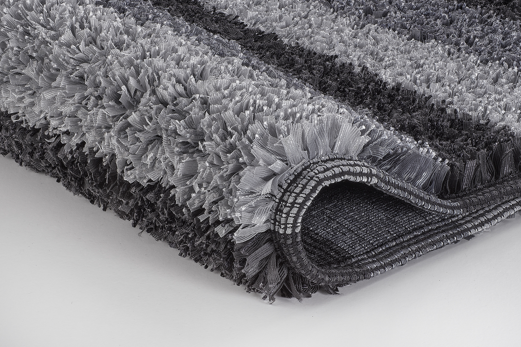 Grauer, flauschiger Teppich mit modernen Streifen, Nahaufnahme der Textur und Kanten.