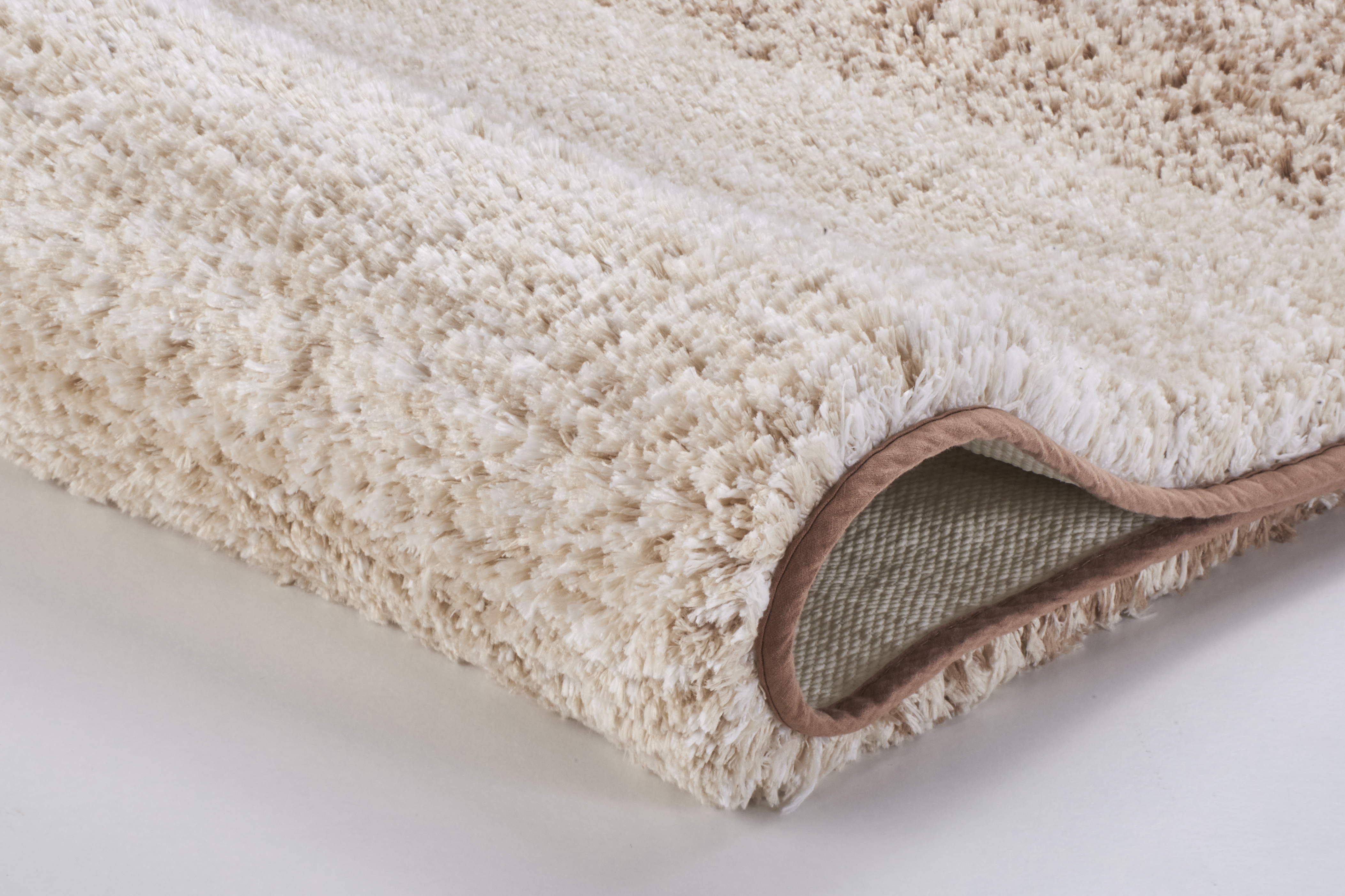 Weicher, cremefarbener Hochflor-Teppich mit rutschfester Unterseite und umsäumten Kanten für gemütliche Wohnräume.