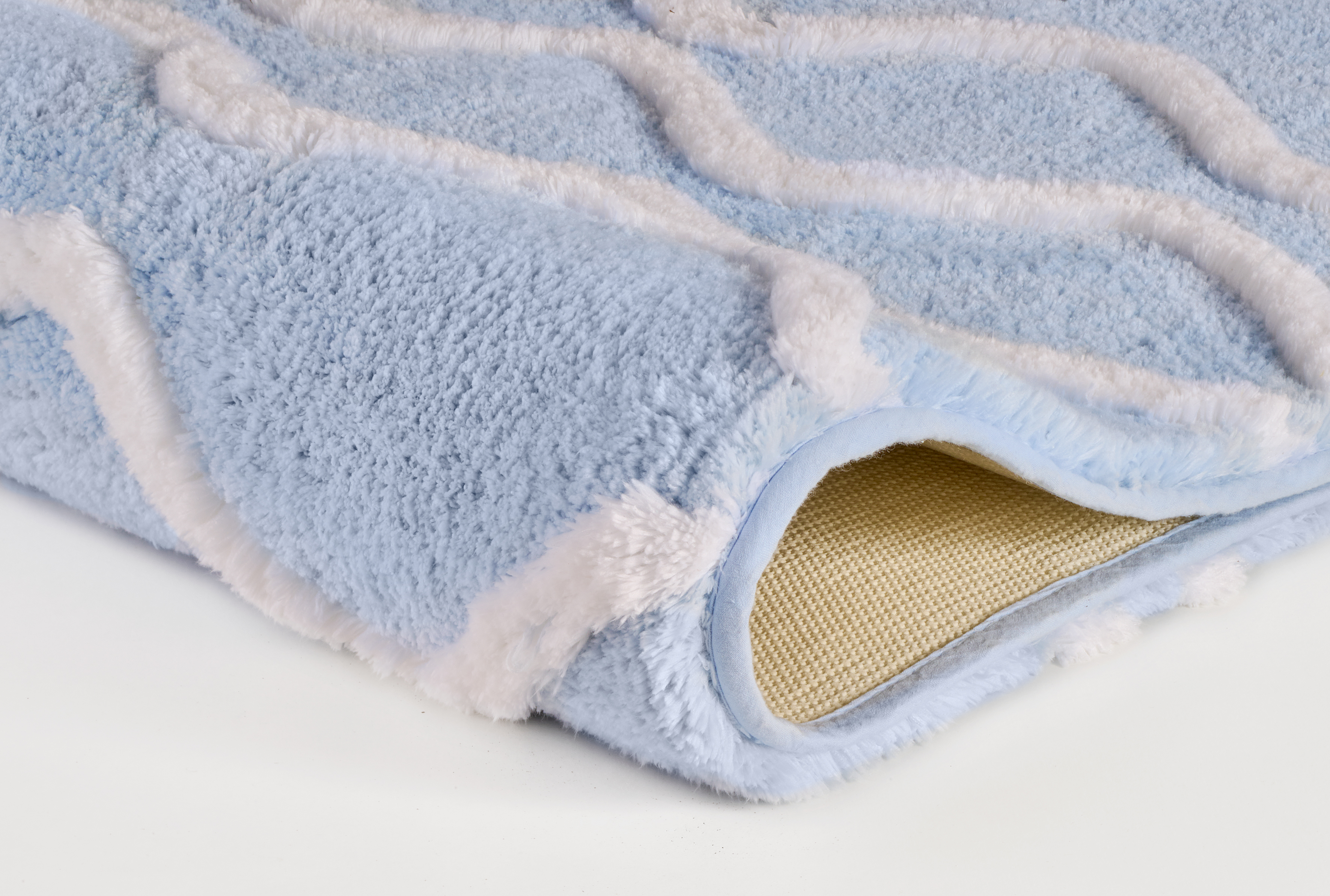 Weicher, hellblauer Teppich mit weißem Wellenmuster und rutschfester Unterseite, ideal für Wohn- und Schlafzimmer.