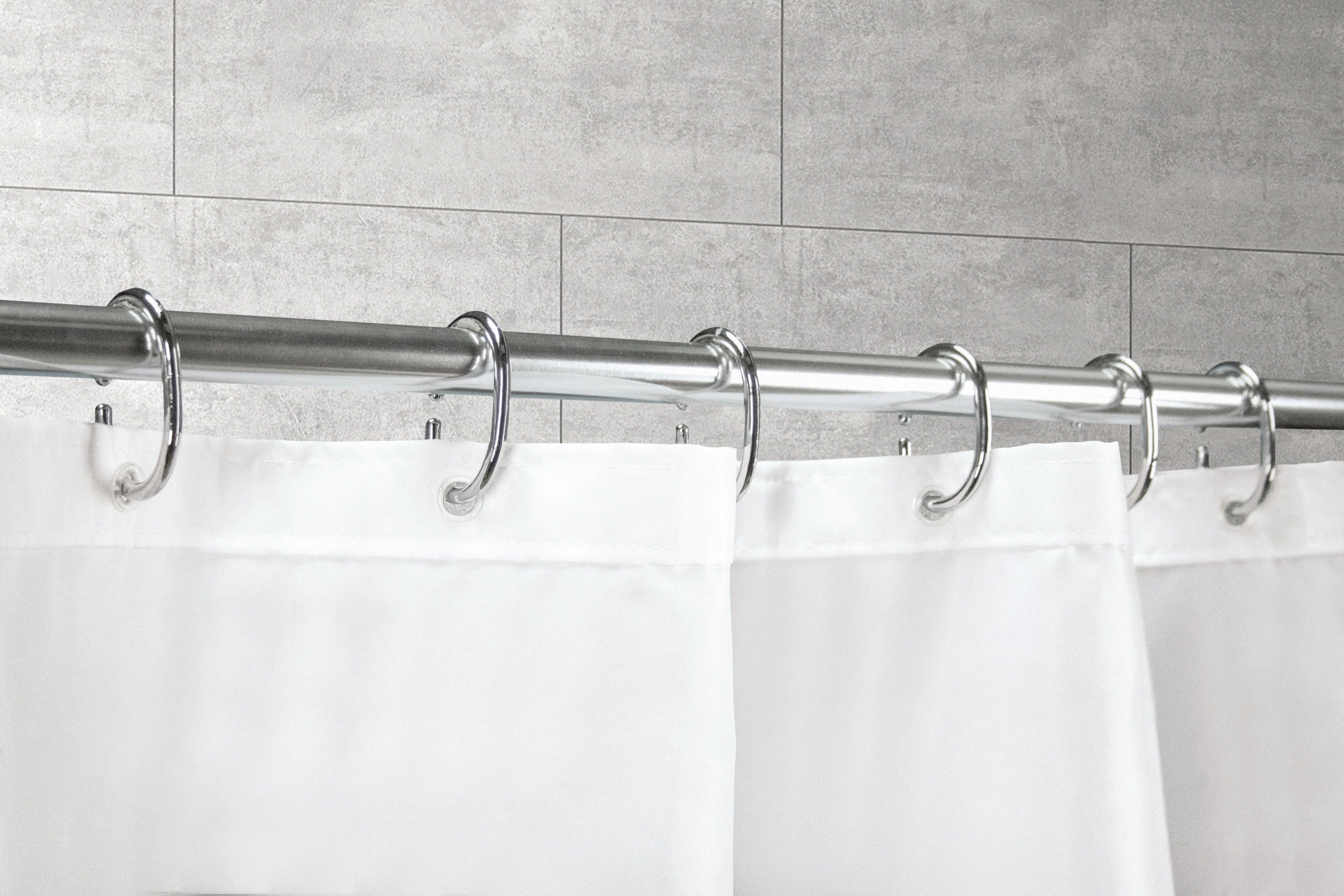 Duschvorhangringe aus silbernem Metall an einer Duschstange, die einen weißen Duschvorhang halten.