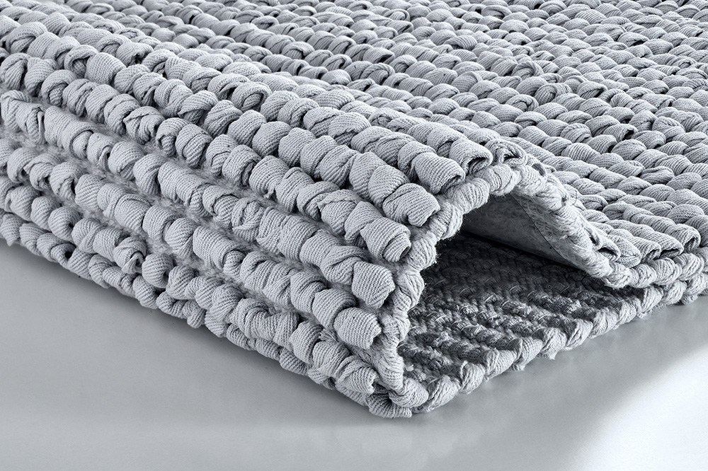 Grauer, gefalteter Badteppich mit strukturierter Oberfläche aus weichem Material, ideal für ein modernes Badezimmer.