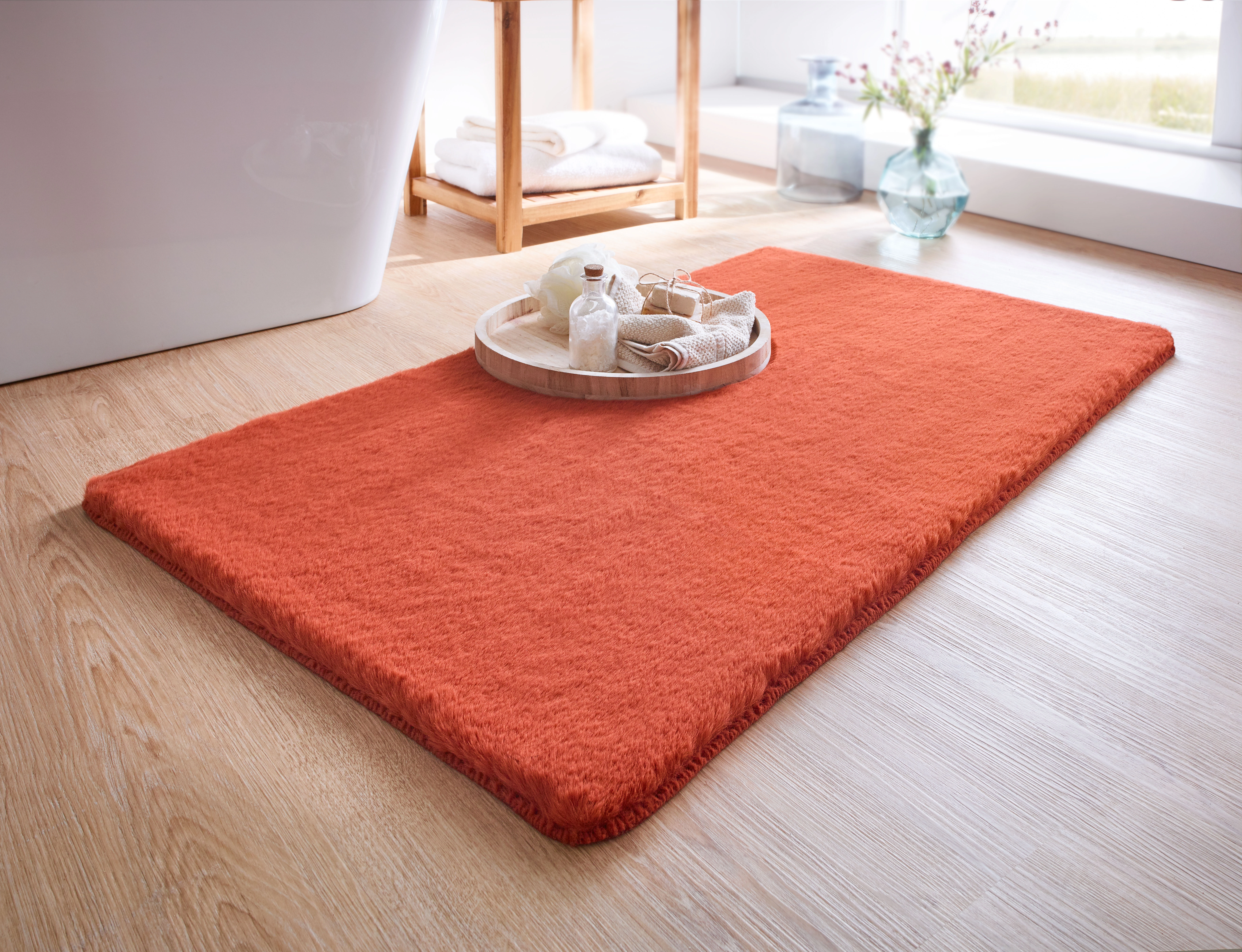 Roter Badezimmerteppich auf Holzfußboden, dekoriert mit einem Tablett voller Badutensilien, im hellen, modernen Badezimmer.