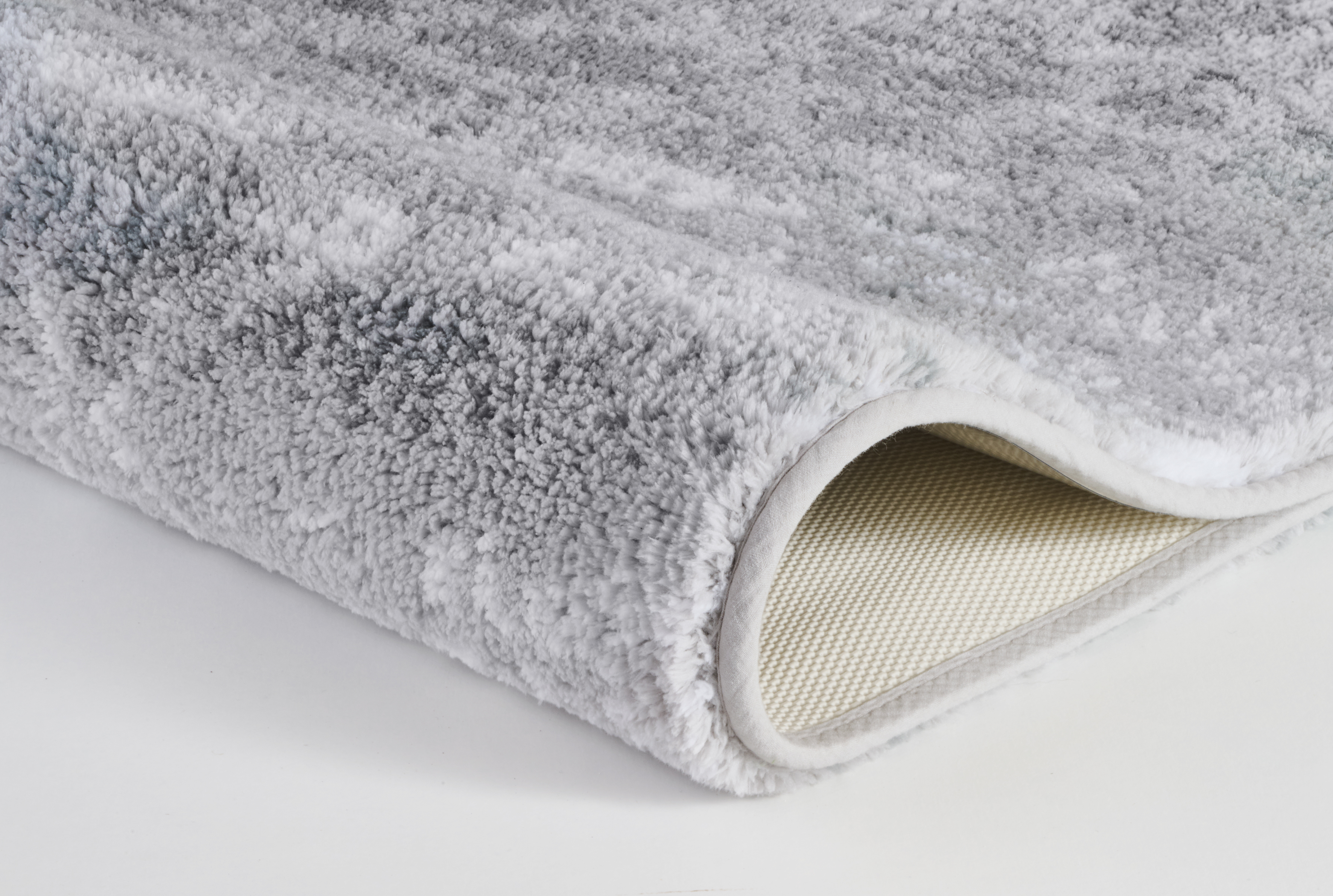 Grauer, flauschiger Teppich mit rutschfester Unterseite, ideal für gemütliche Wohnräume.