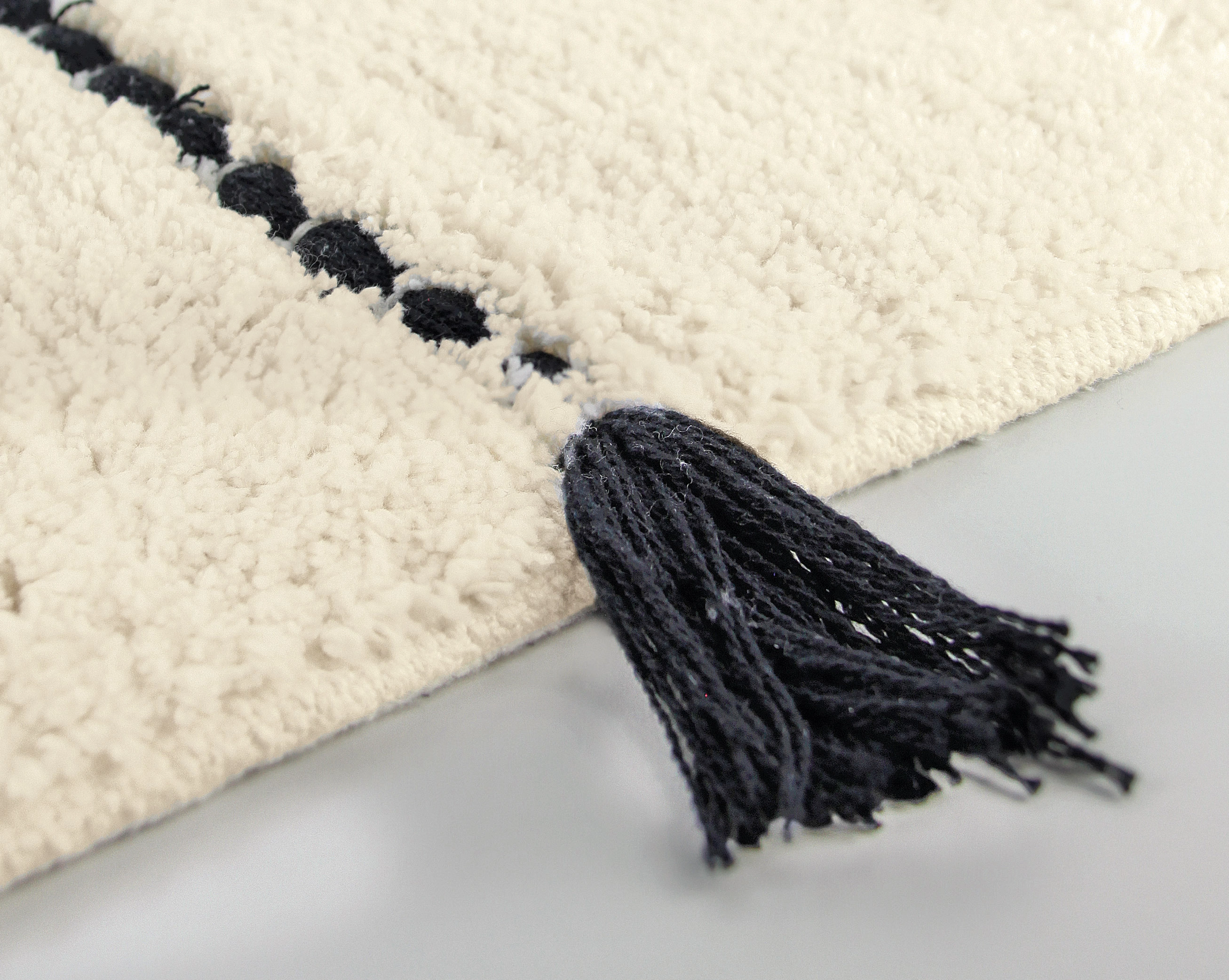 Weißer Teppich mit schwarzem Quasten-Detail und schwarzem Streifenmuster.