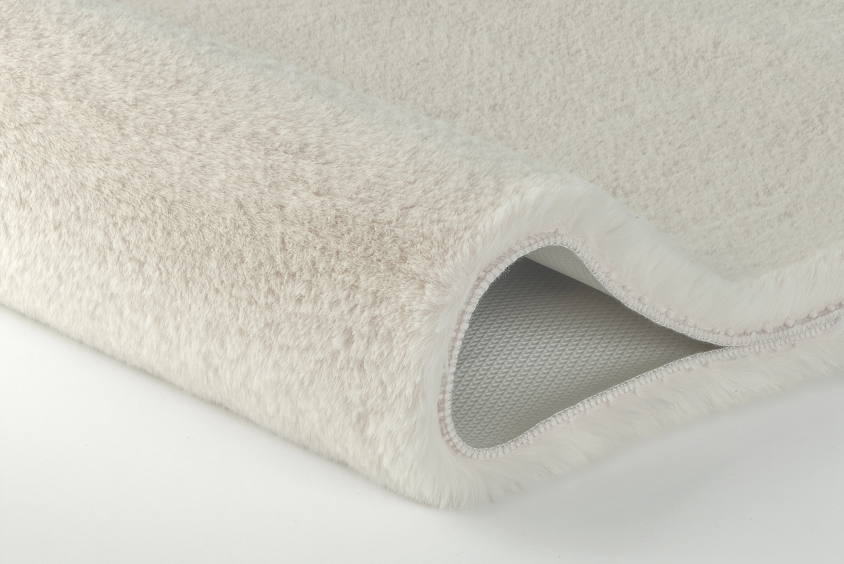 Weißer, flauschiger Teppich mit rutschfester Unterseite, ideal für gemütliche Wohnräume.