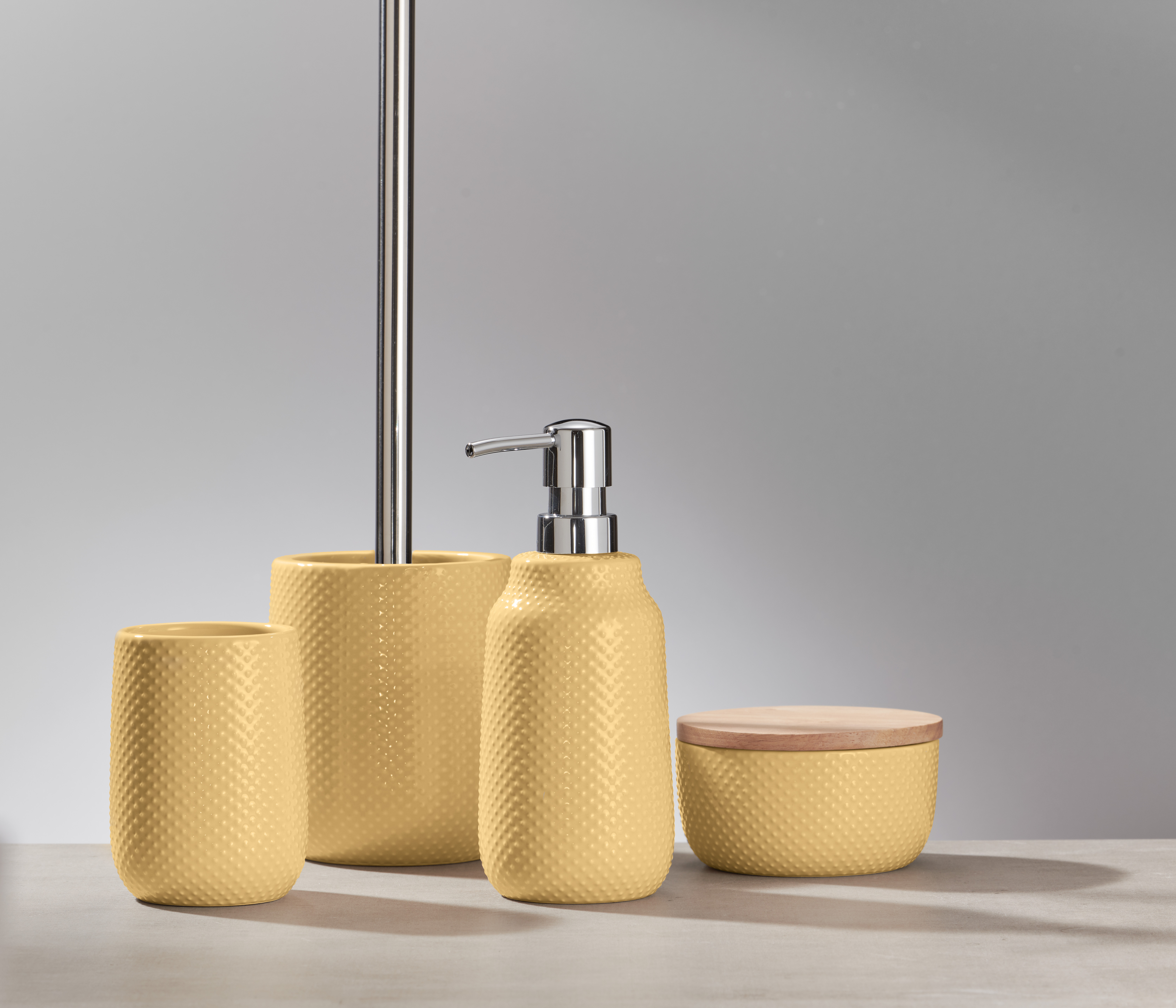 Set aus gelben Badaccessoires mit strukturierter Oberfläche, bestehend aus Seifenspender, Becher, Dose und WC-Bürstenhalter.