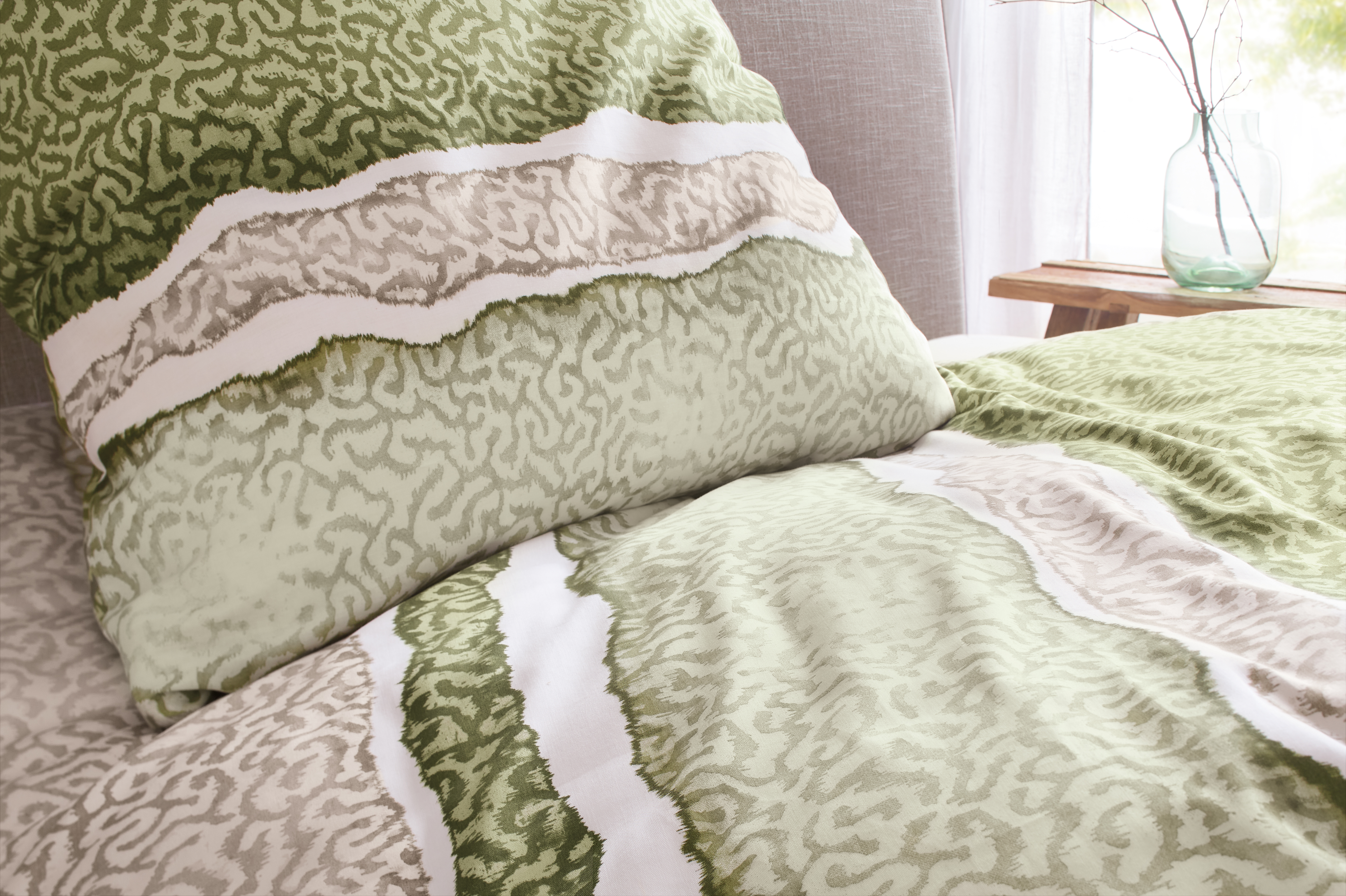 Bettwäsche-Set mit grünem und beigem Muster, weiche Textur, dekorativ auf einem Bett arrangiert, modernes Design.
