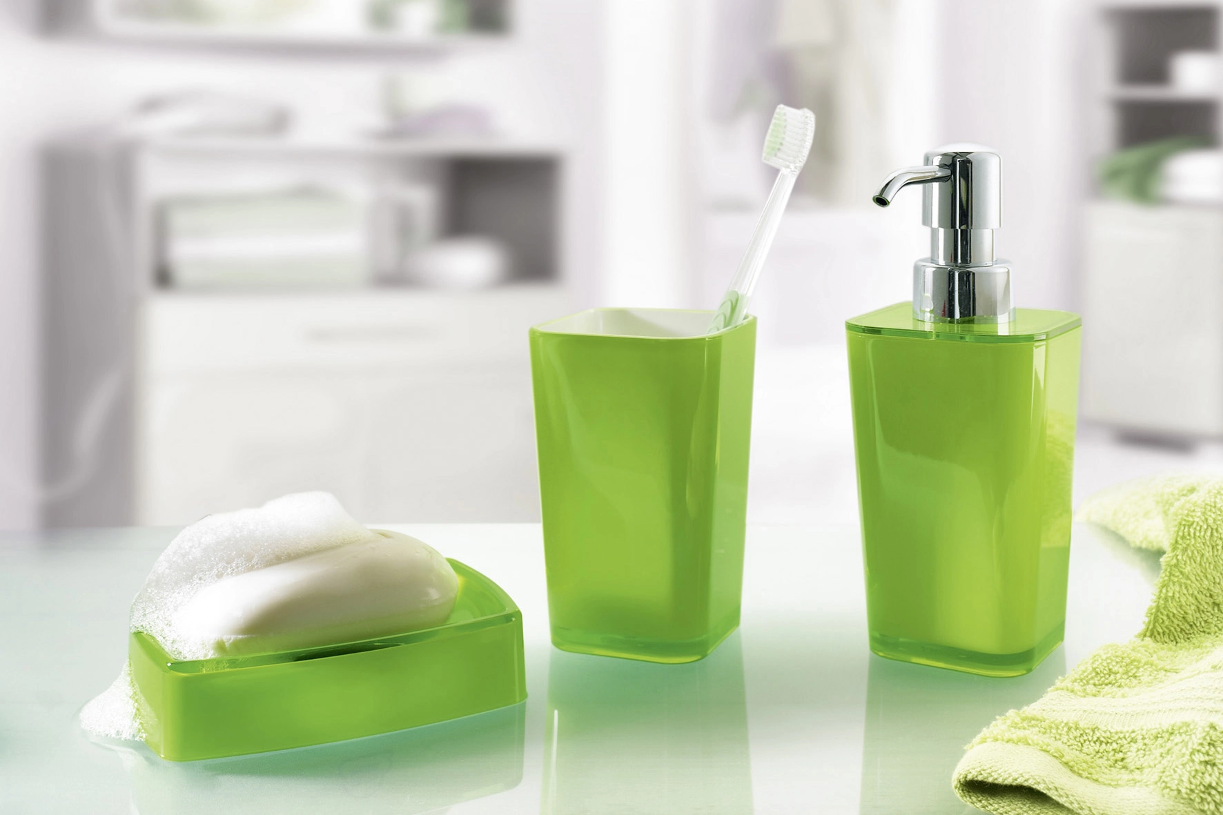 Grünes Badezimmer-Set mit Seifenschale, Zahnbürstenhalter und Seifenspender auf einem weißen Waschtisch.