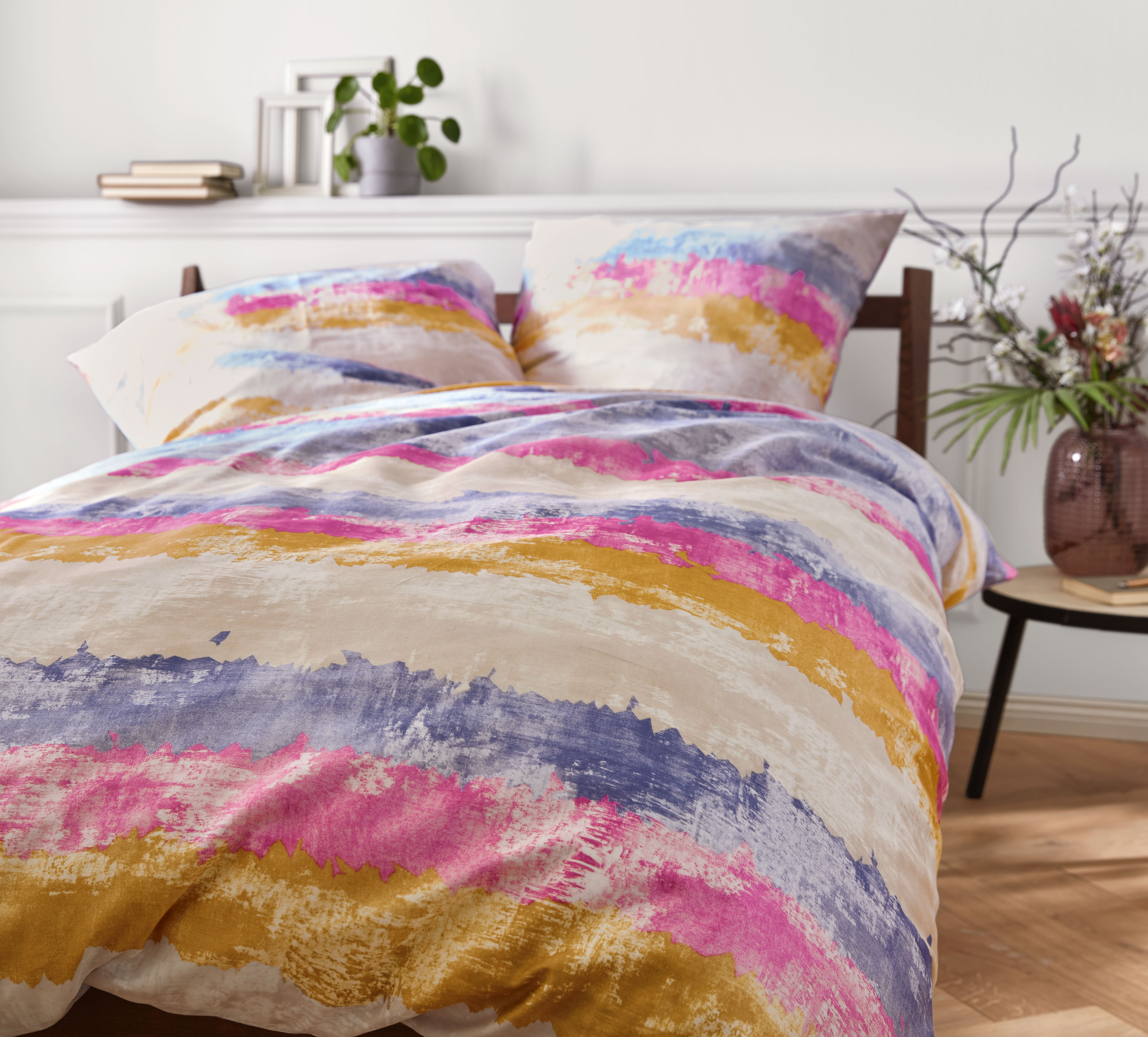 Bunte Bettwäsche mit abstraktem Streifenmuster in Rosa, Blau und Gelb auf einem gemütlichen Bett in modernem Schlafzimmer.