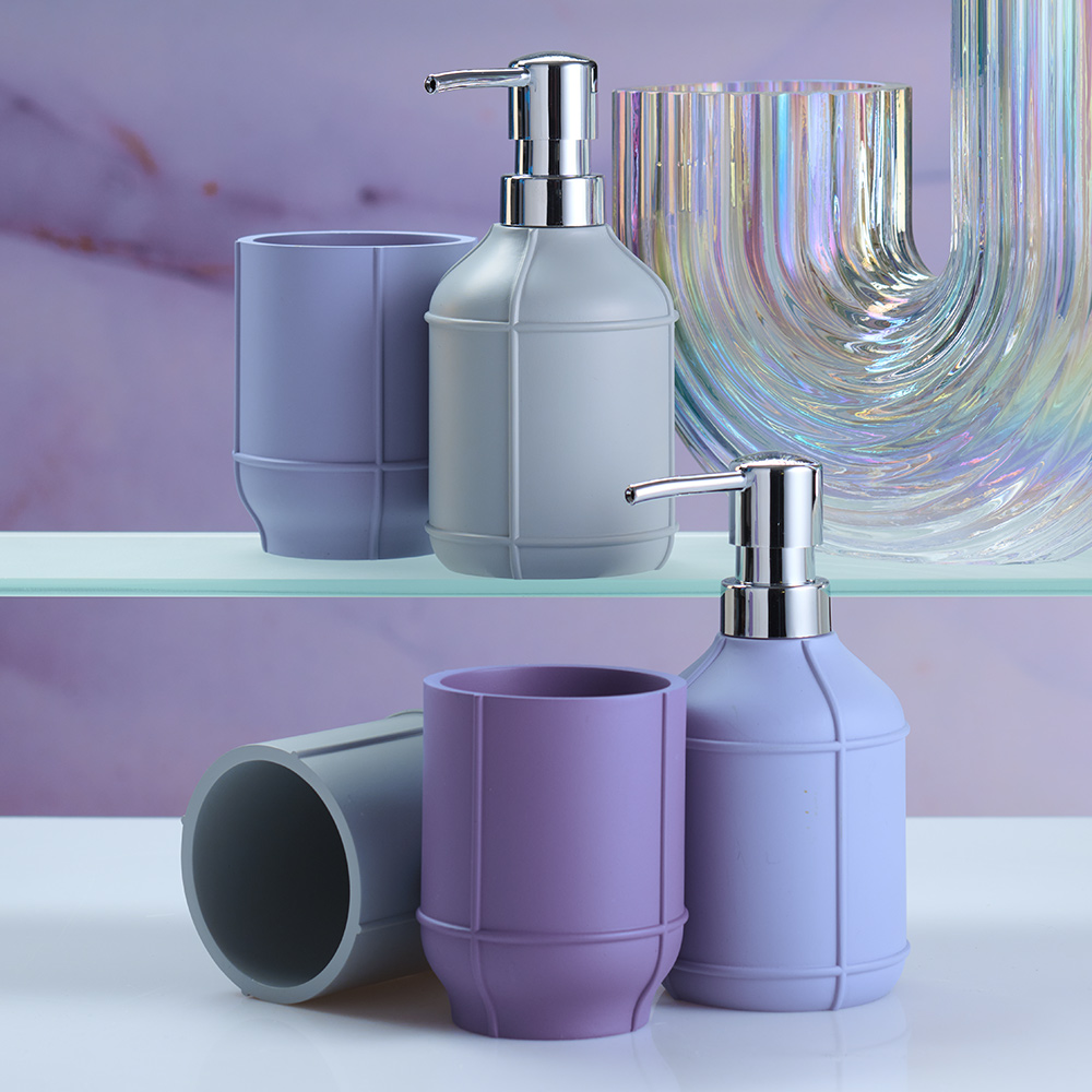 Seifenspender und Zahnputzbecher in Pastellfarben auf Glasregal vor lila Hintergrund, modernes und stilvolles Badezimmer-Set.