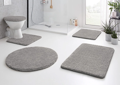 Graue Badematten-Set in modernem Badezimmer mit Dusche, WC und Pflanzen.