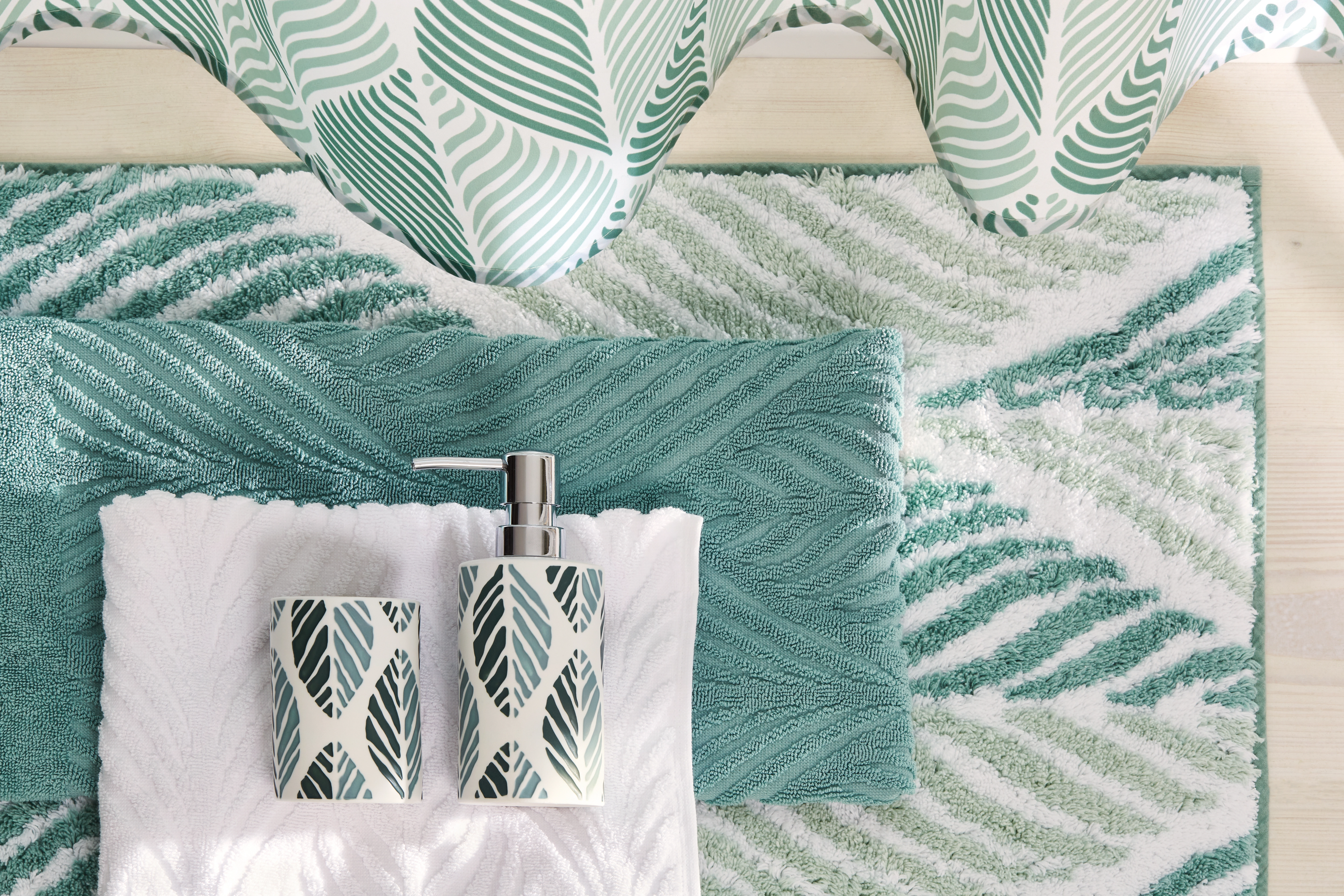 Badezimmer-Set mit grün-weißem Blattmuster, bestehend aus Seifenspender, Zahnputzbecher, Handtuch und Badematte.