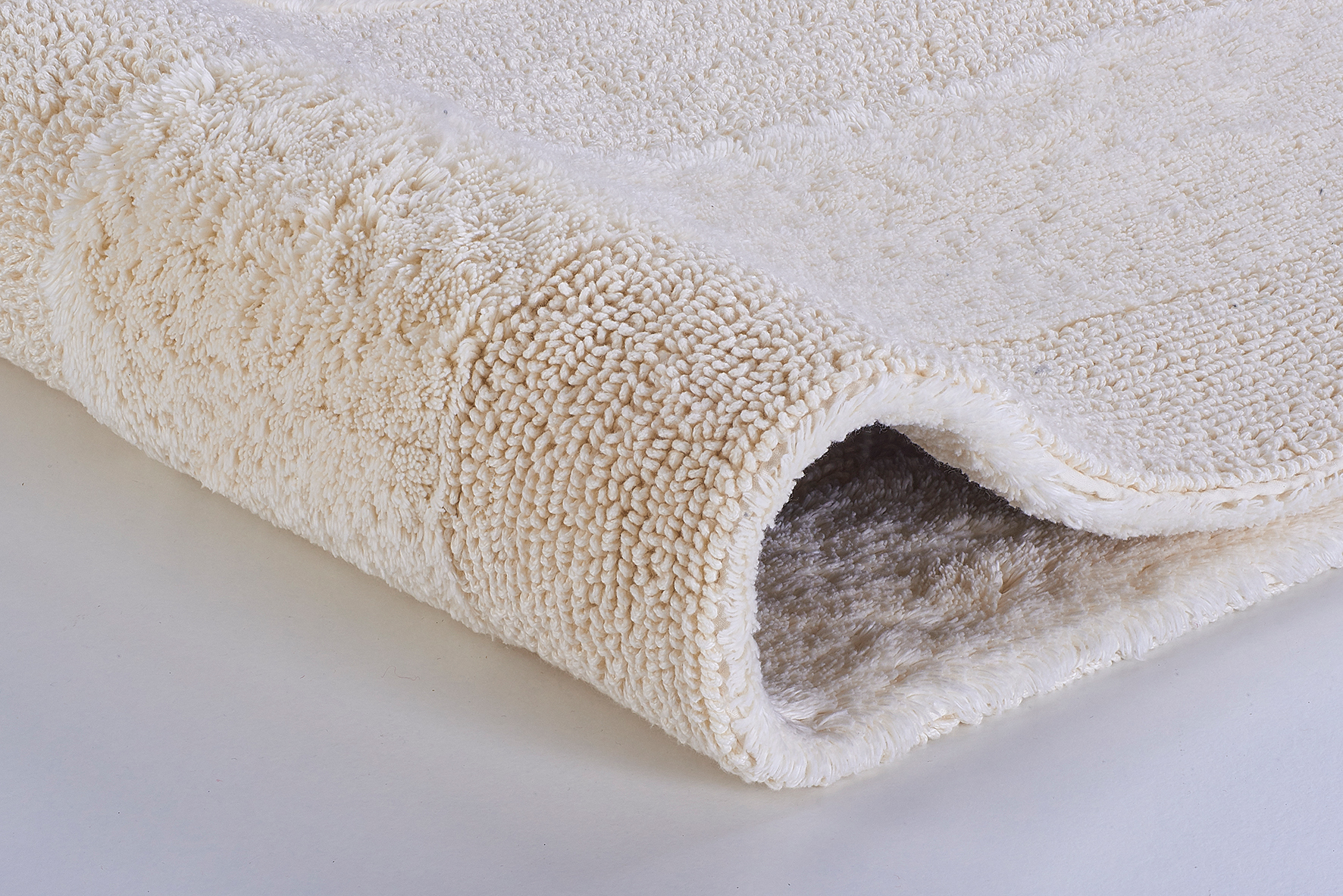 Weicher, cremefarbener Badteppich mit flauschiger Oberfläche und rutschfester Unterseite, ideal für ein gemütliches Badezimmer.