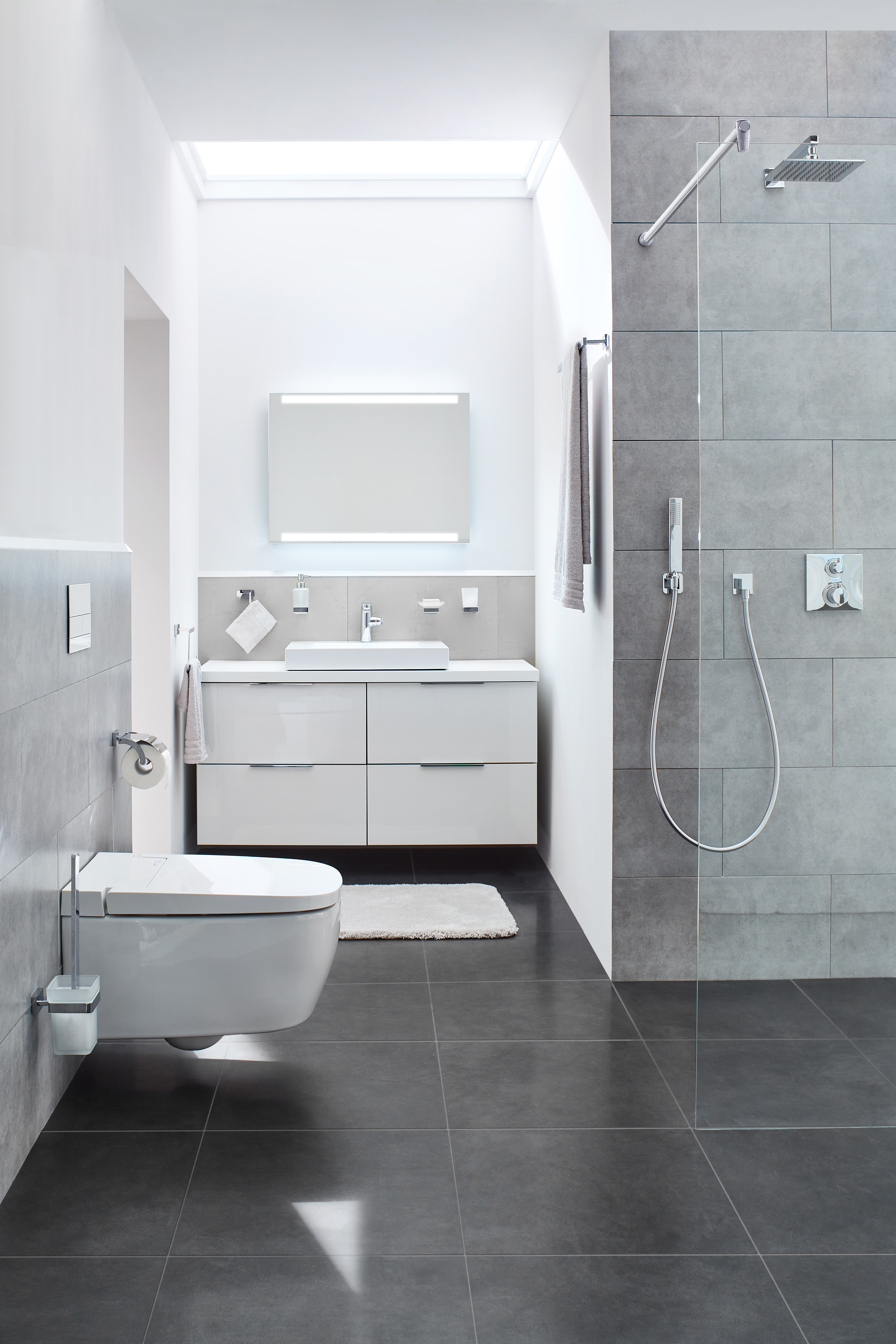 Modernes Badezimmer mit grauen Fliesen, weißem Waschtisch, wandhängender Toilette und offener Regendusche.