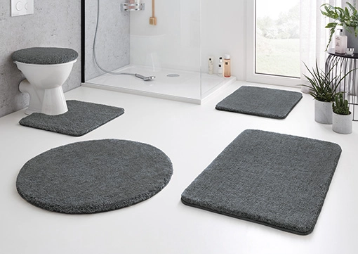 Graues Badezimmerteppich-Set aus weichem Material, bestehend aus WC-Deckelbezug, Duschvorleger und zwei rechteckigen Matten.