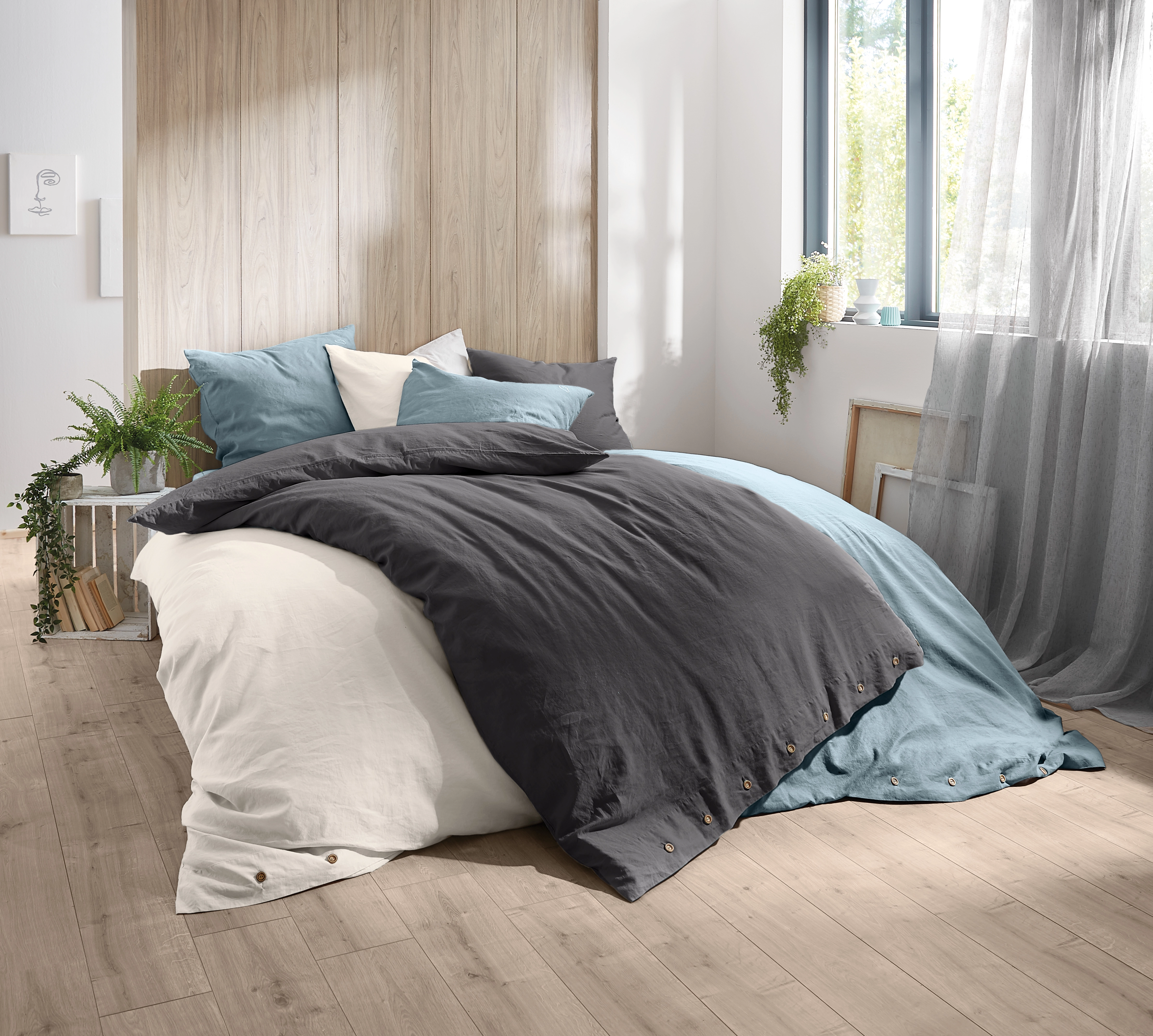 Bettwäsche-Set in Grau und Blau, gemütlich arrangiert in modernem Schlafzimmer mit Holz- und Pflanzenakzenten.