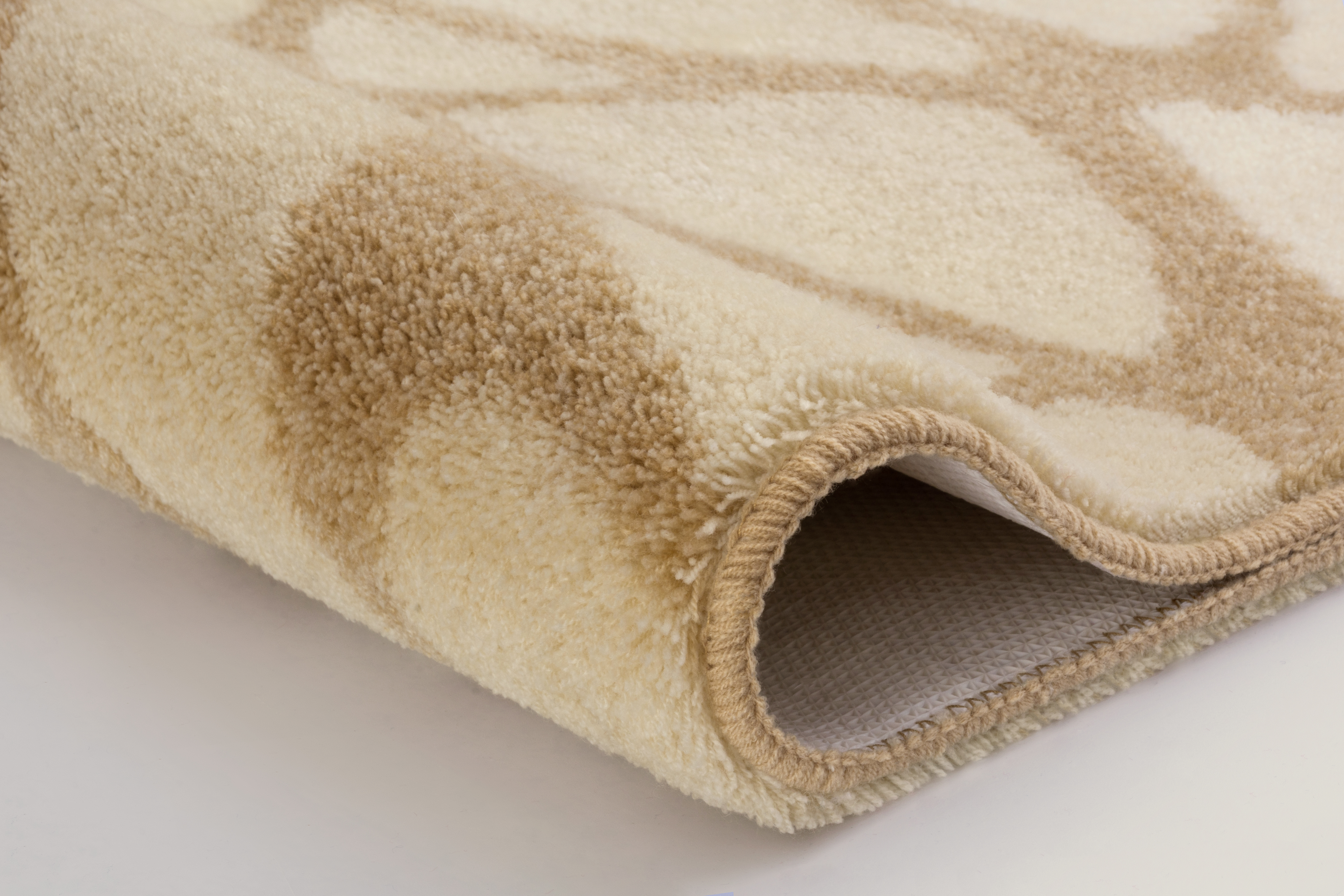 Beige-weißer Teppich mit weichem Flor und dezentem Muster, eingerollt und detailreich fotografiert.