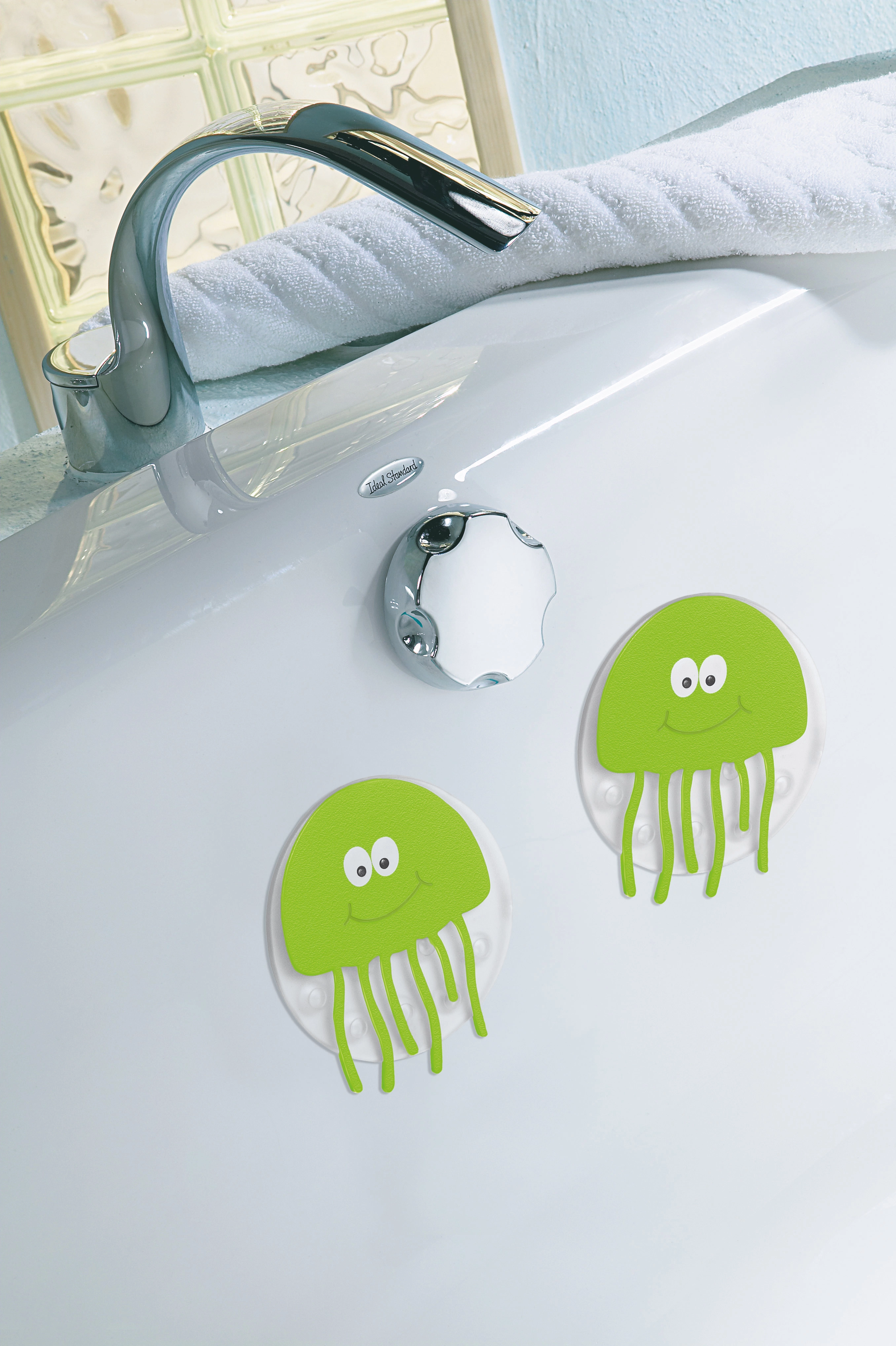 Zwei grüne, lächelnde Quallen-Badewannenmatten an einer weißen Badewanne, im Hintergrund ein Wasserhahn und ein Handtuch.