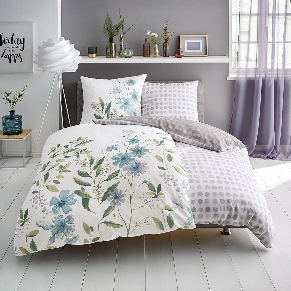 Bettwäsche-Set mit floralem Muster in Blau und Grün, kombiniert mit grauen Punkten, auf modernem Bett in hellem Raum.