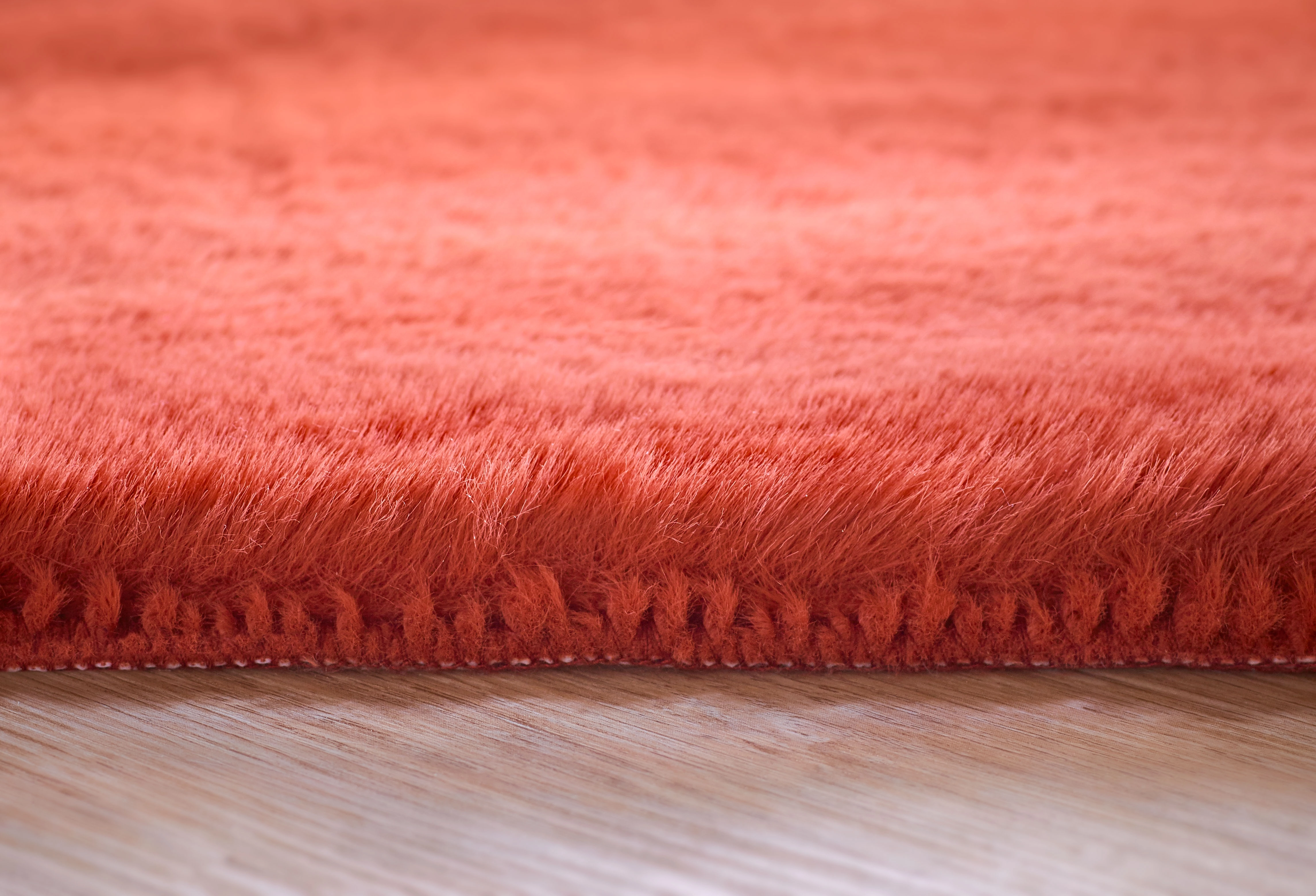 Weicher, flauschiger, orangefarbener Teppich auf einem Holzboden, Nahaufnahme der Textur und Kanten.