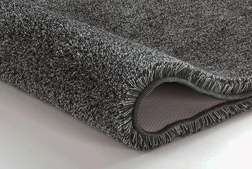 Grauer, flauschiger Teppich mit rutschfester Unterseite, ideal für Badezimmer und Wohnräume.