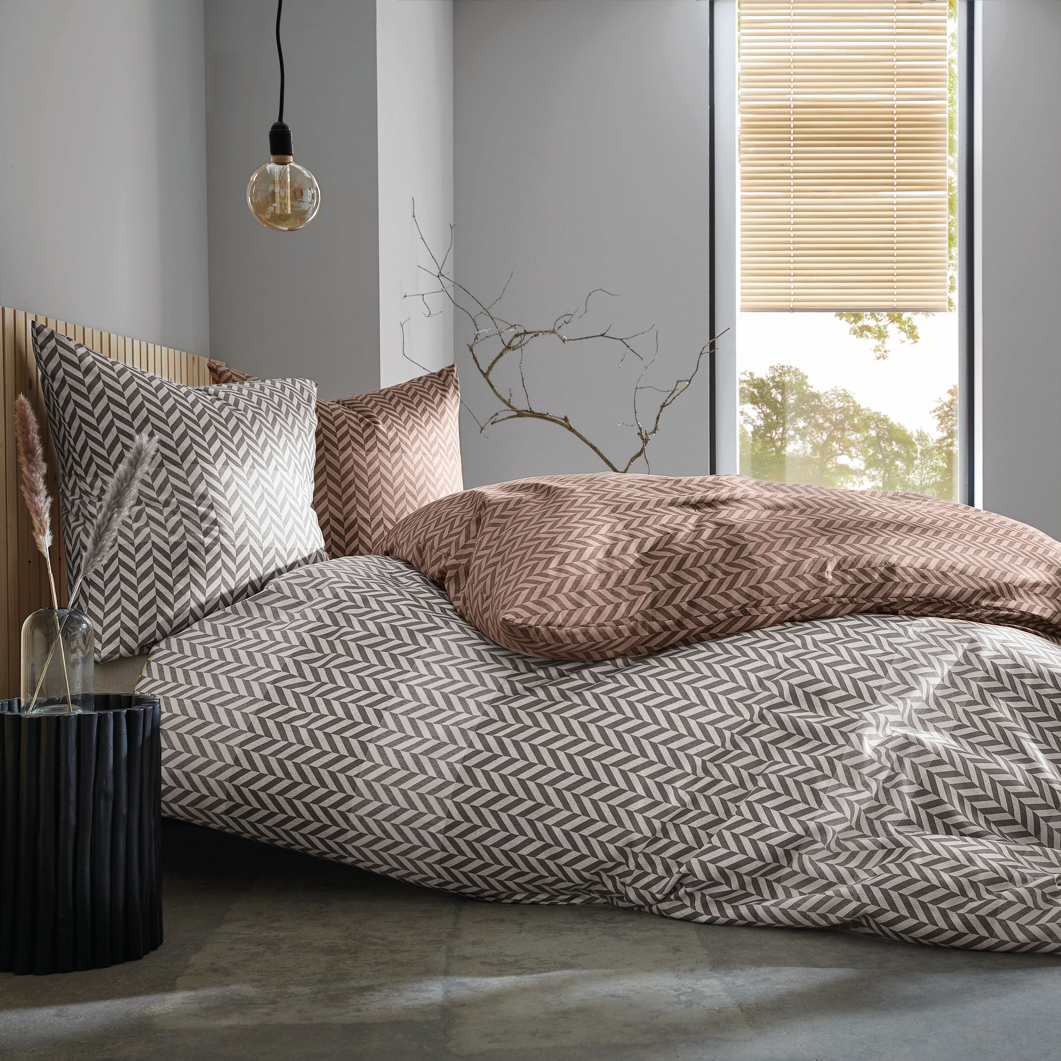 Bettwäsche-Set mit Zickzack-Muster in Braun und Grau, modernes Schlafzimmer, hängende Glühbirne, Fenster mit Jalousien.