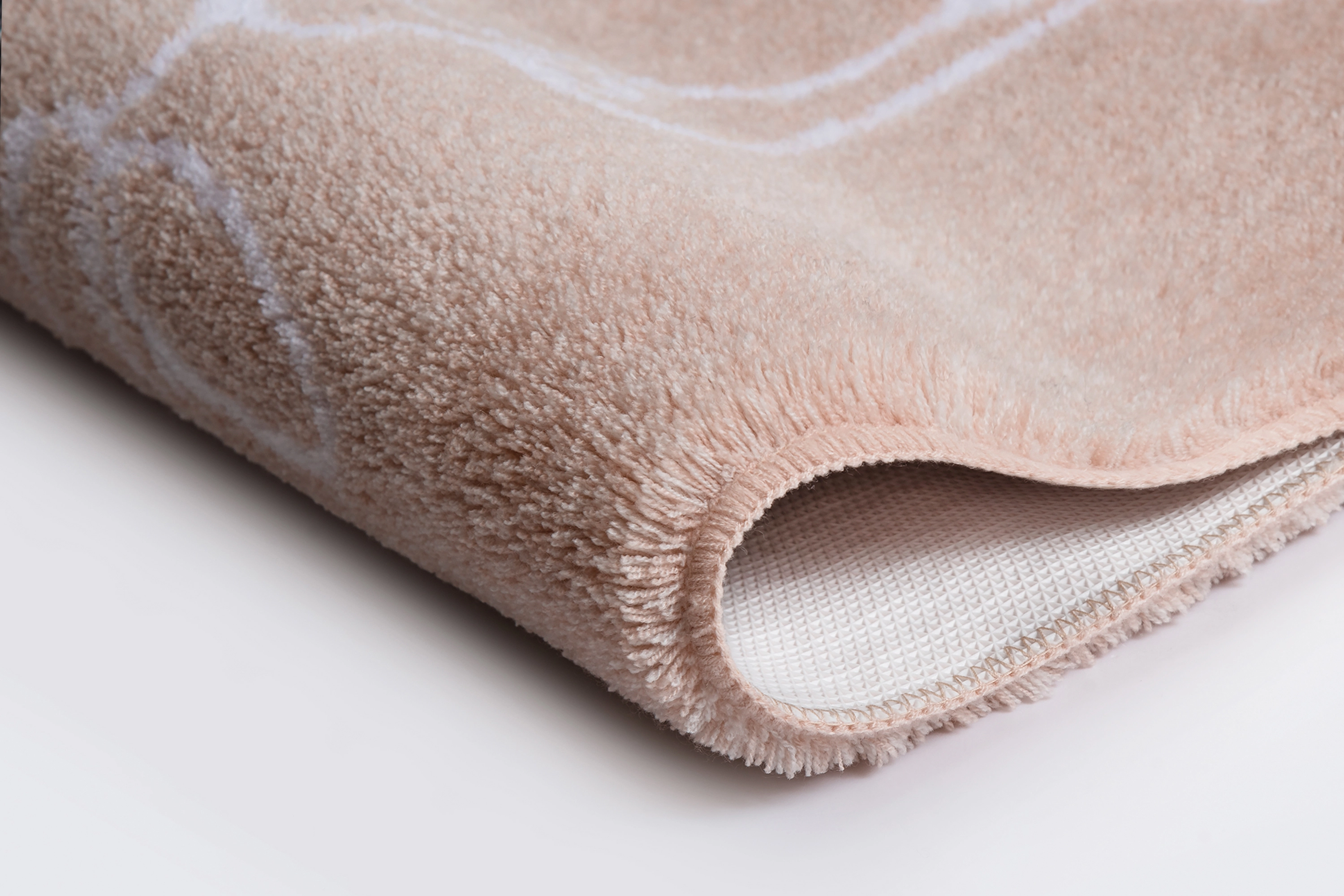 Weicher, beiger Teppich mit dezentem Muster, Nahaufnahme der Kante und Textur. Ideal für gemütliche Wohnräume.